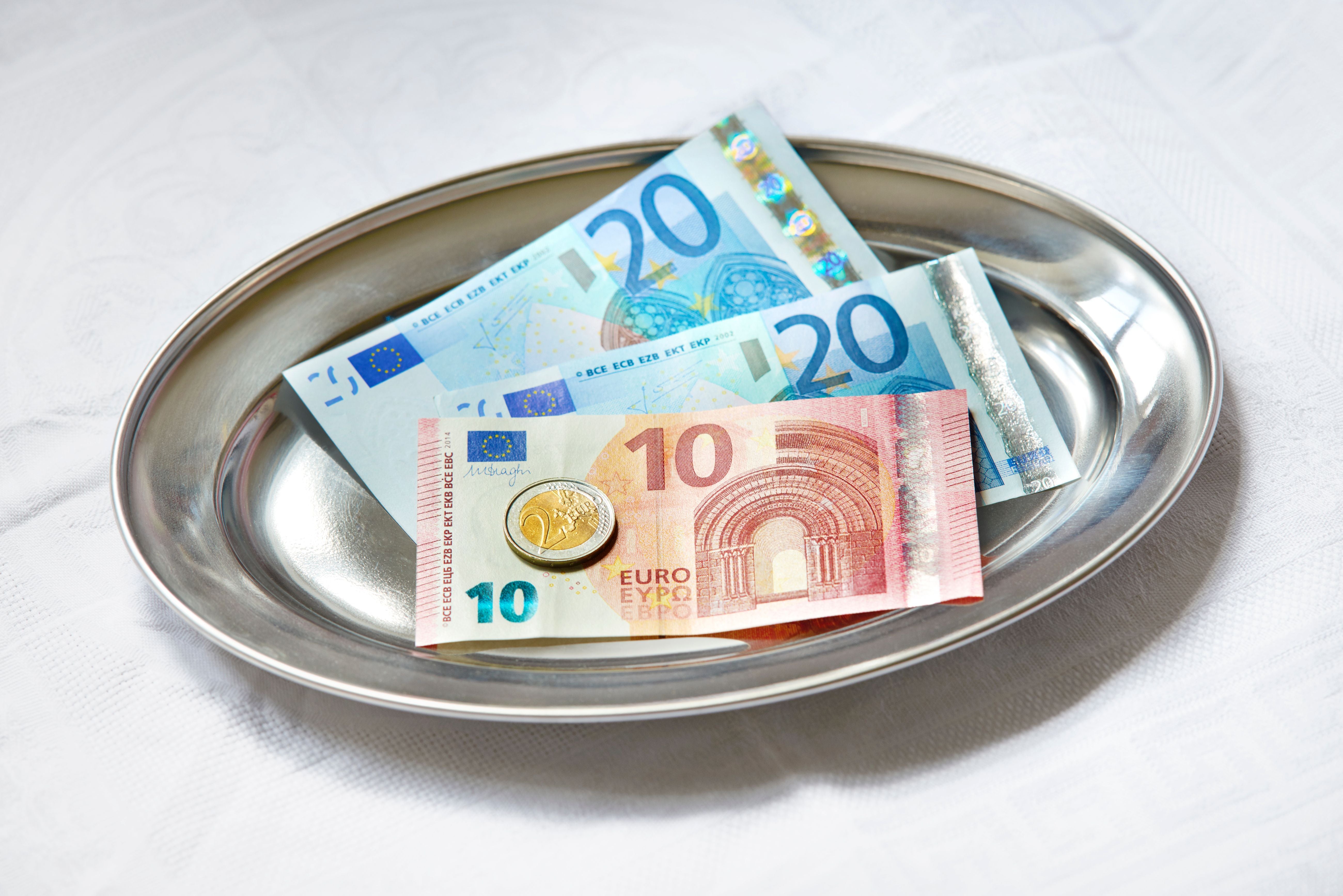 Trinkgeld aus Euro-Scheinen und Münzen auf einem silbernen Tablett.