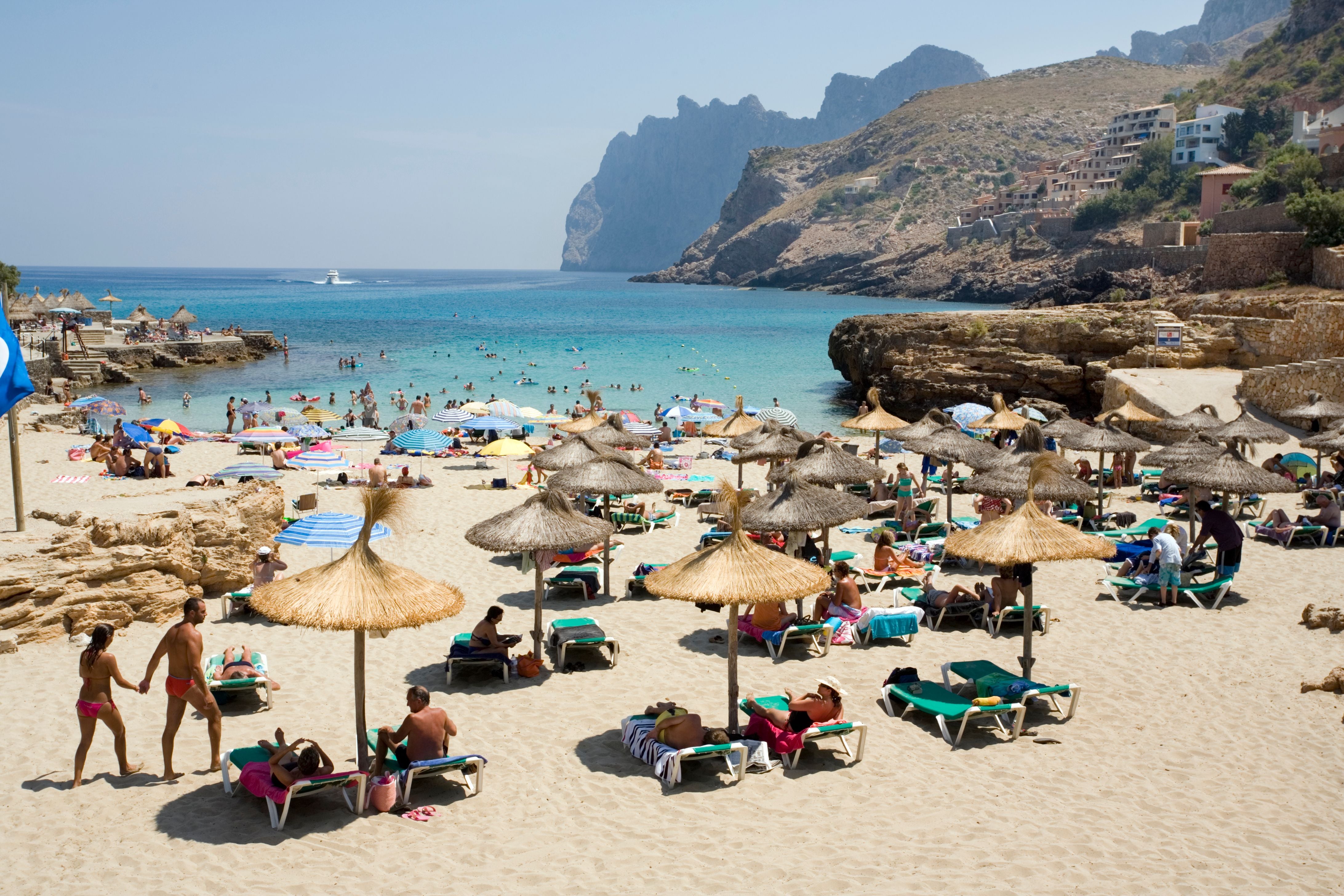 Voller Sandstrand auf Mallorca mit Sonnenschirmen, Liegen und vielen Menschen am Meer.