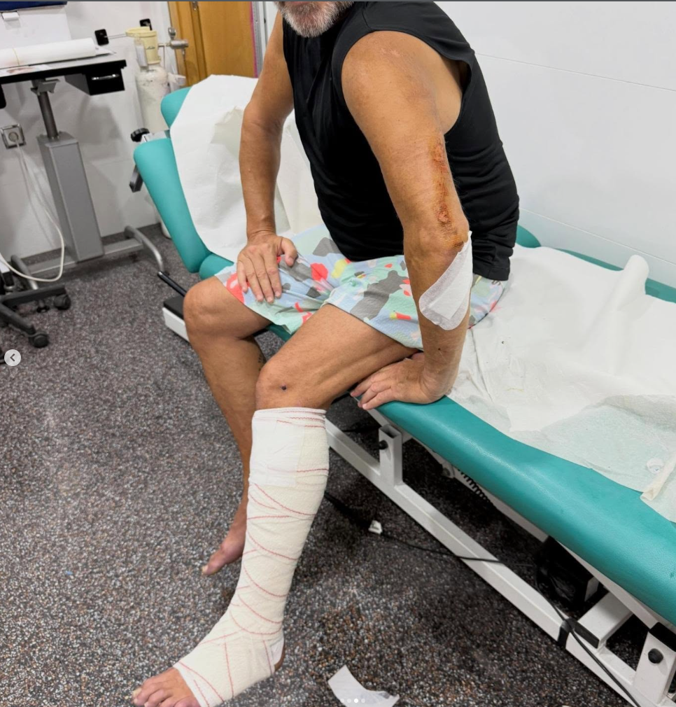 Ein Mann mit Schürfwunden am Arm und Verband am Bein sitzt auf einer Untersuchungsliege.