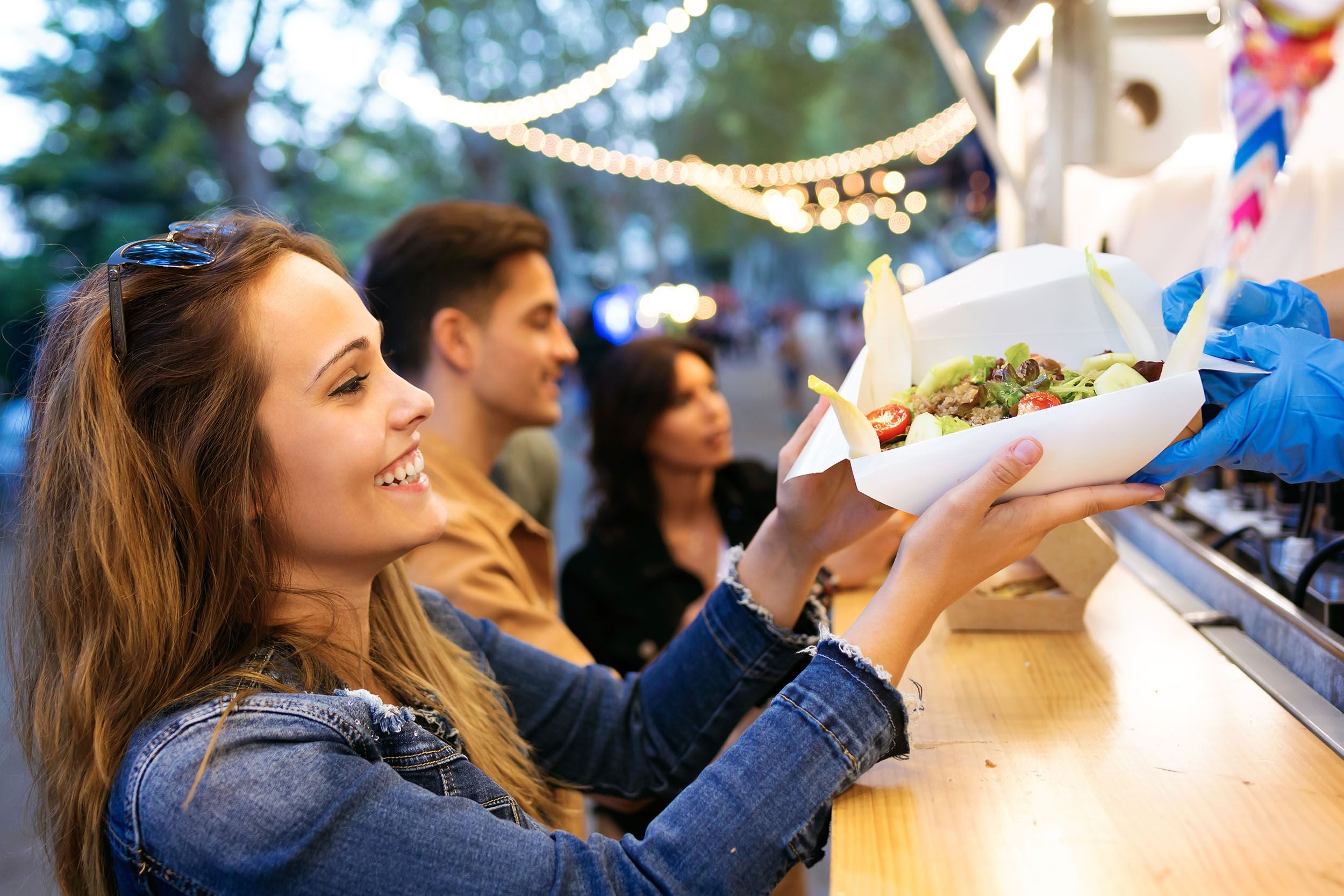 Junge Frau bekommt frisches Essen an einem Foodtruck und lächelt dabei glücklich.