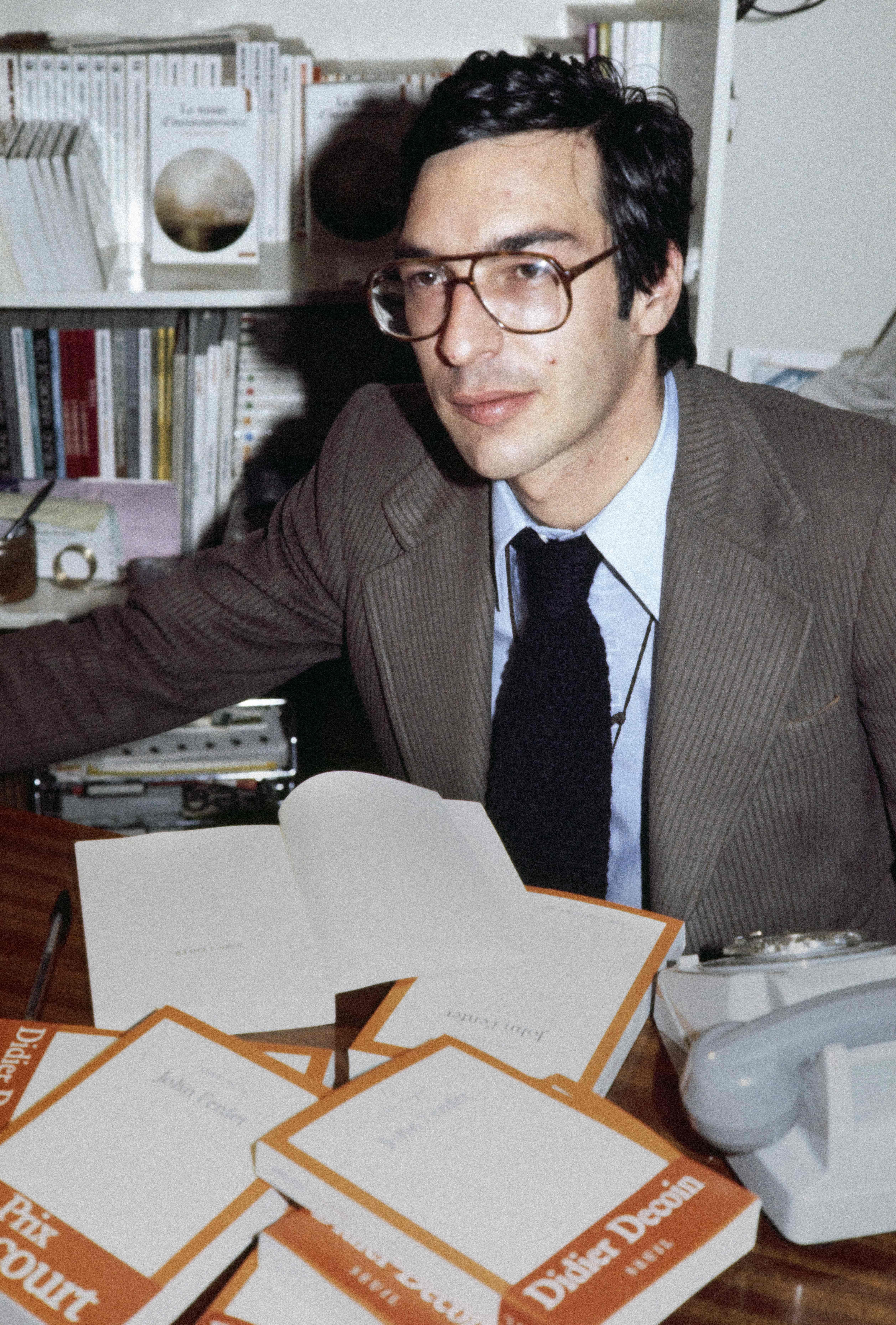 Ein Mann mit Brille sitzt am Schreibtisch mit mehreren Büchern und schaut zur Seite.