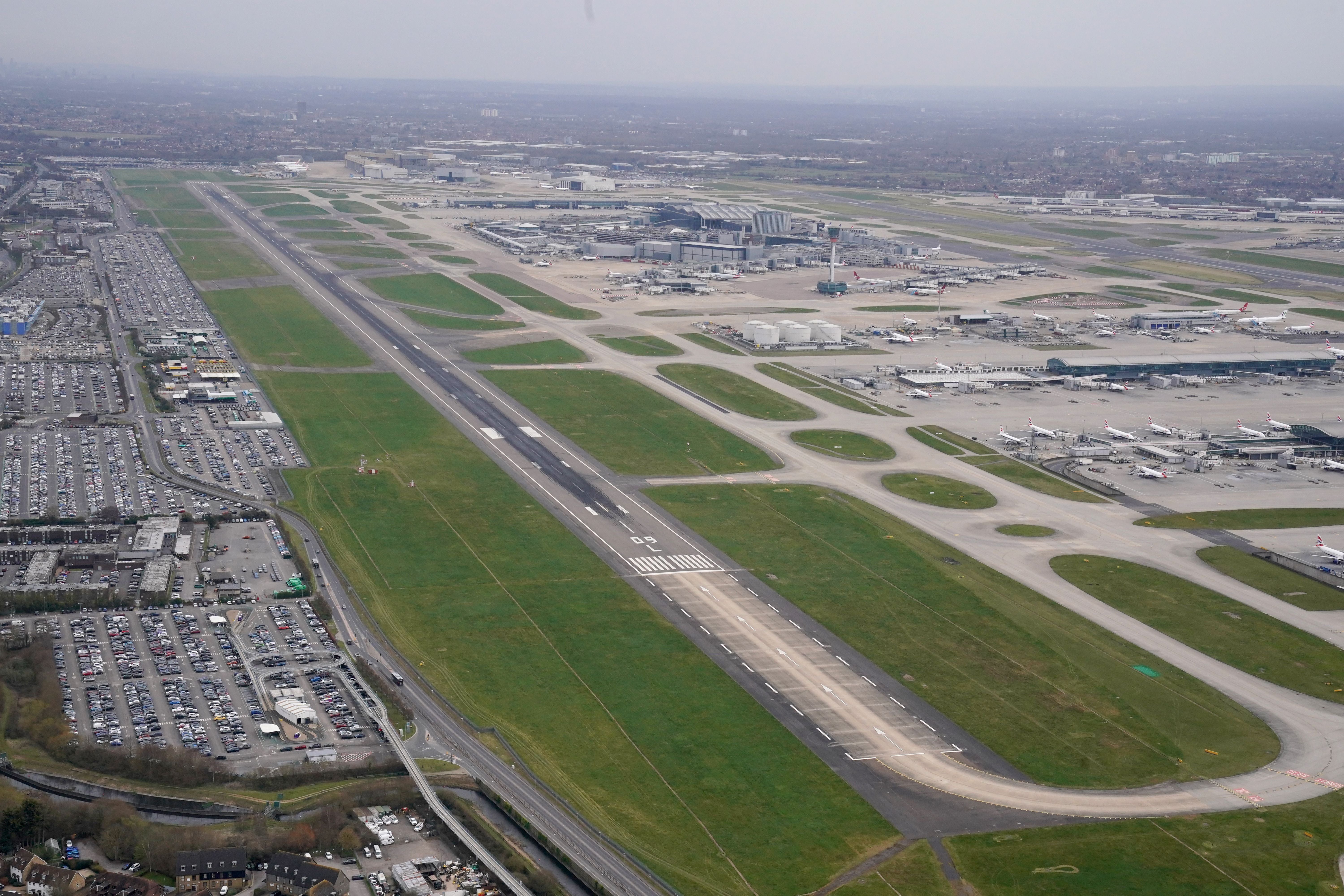 Leere Start- und Landebahn am Flughafen Heathrow mit geparkten Flugzeugen im Hintergrund.