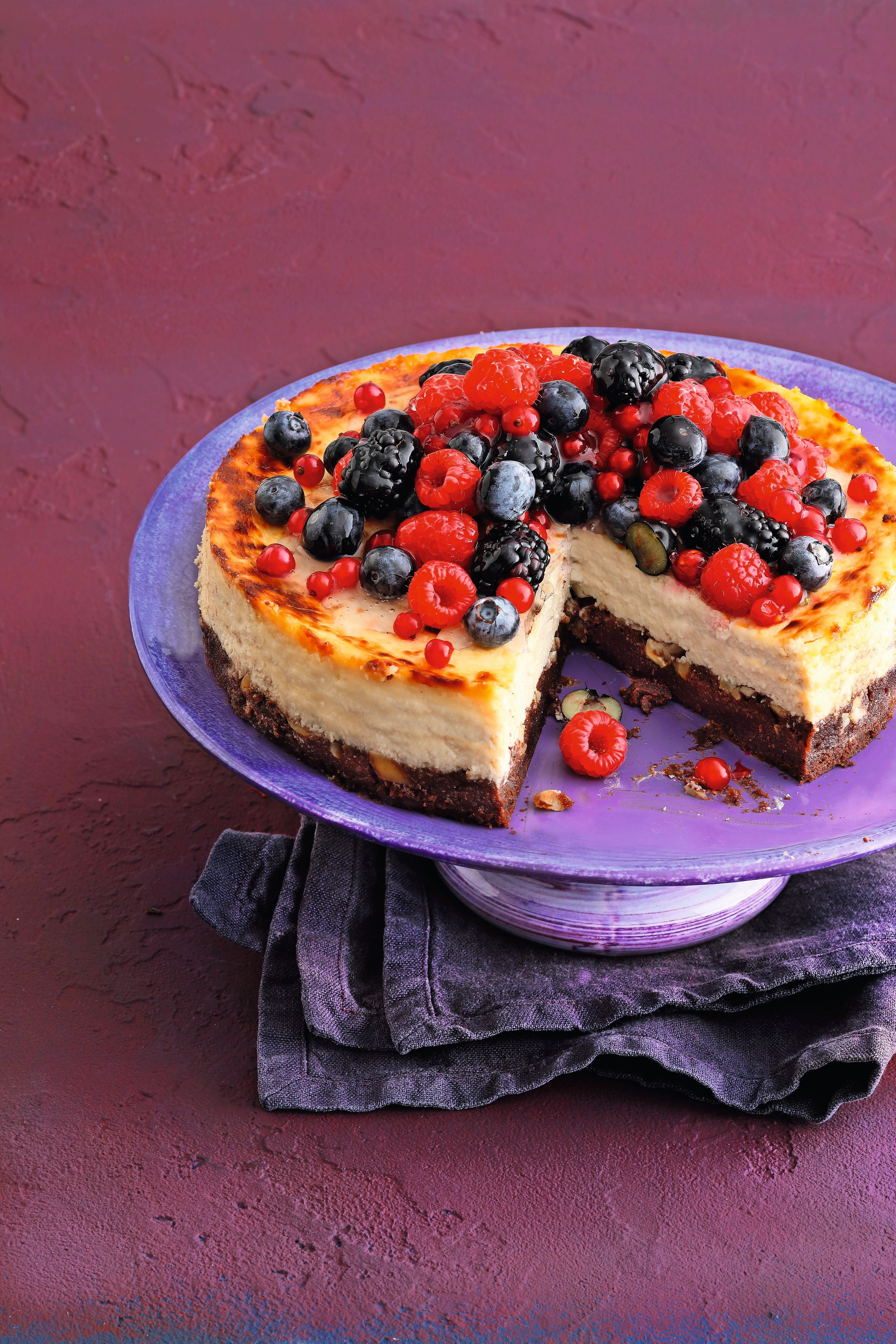 Beeren-Cheesecake mit Brownie-Boden auf einer Platte, mit frischen Beeren garniert.