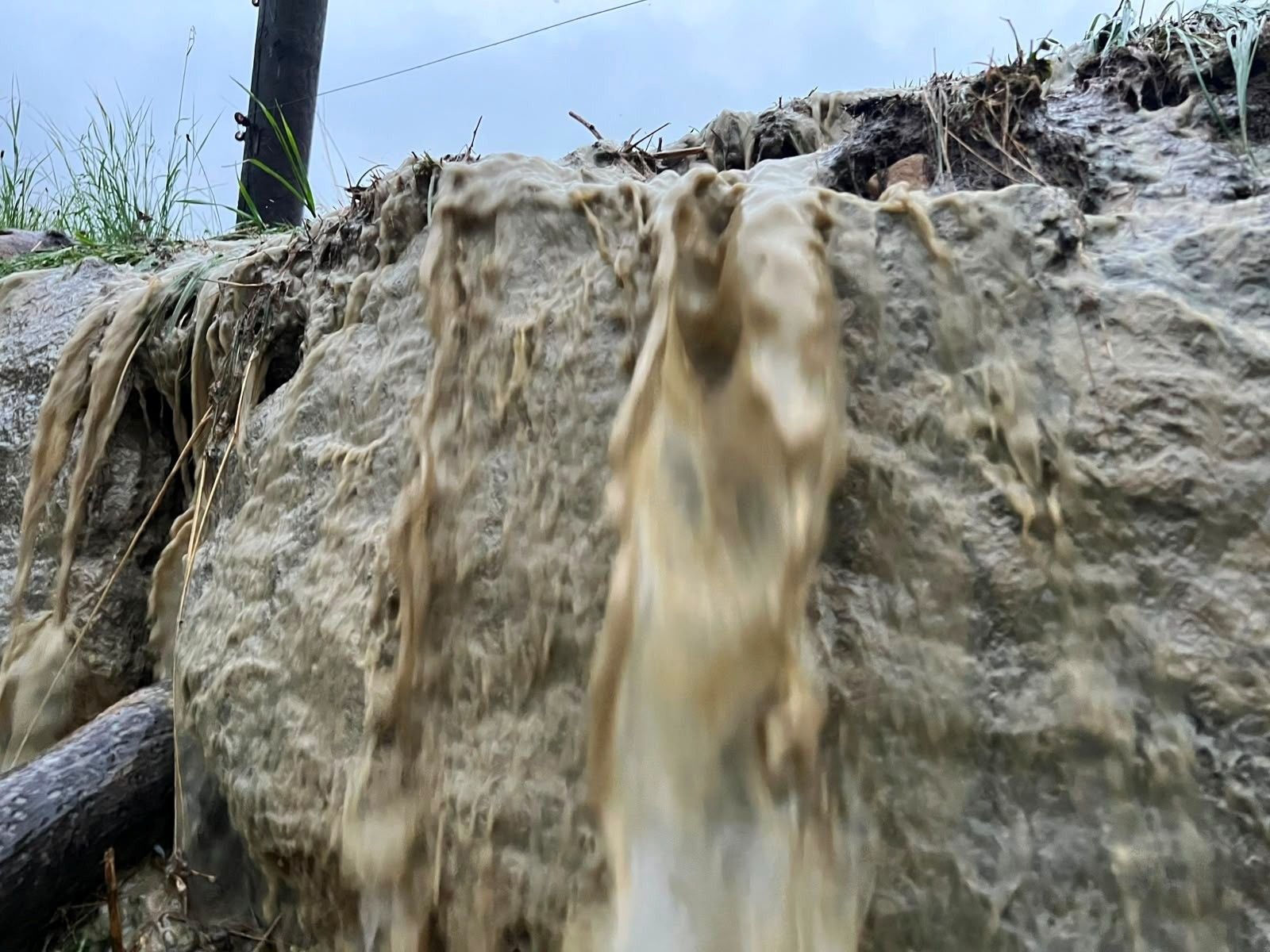 Schmutziges Regenwasser fließt über einen steinigen Abhang mit etwas Gras am Rand.