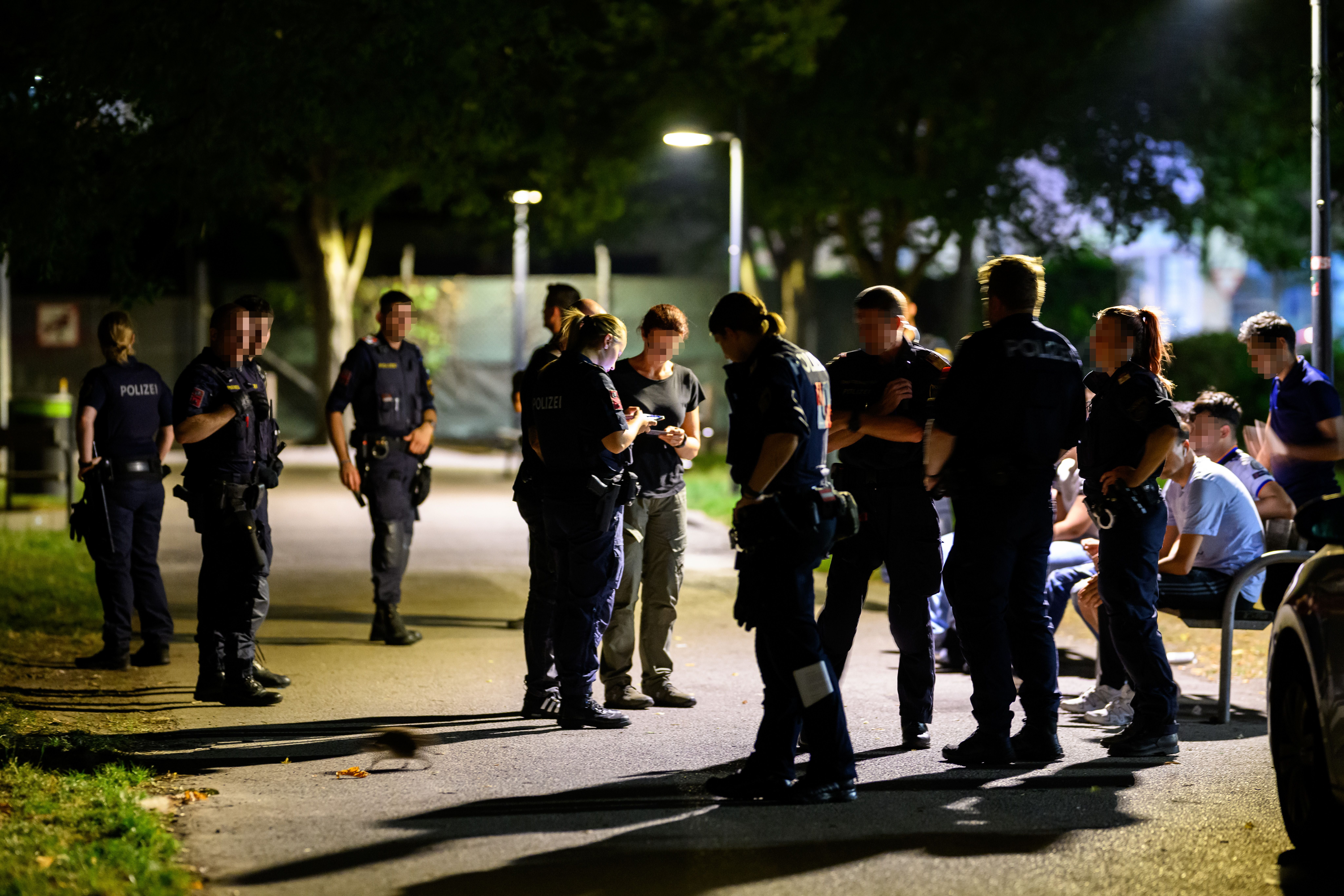 Mehrere Polizisten kontrollieren nachts Passanten in einem Park in Wien.