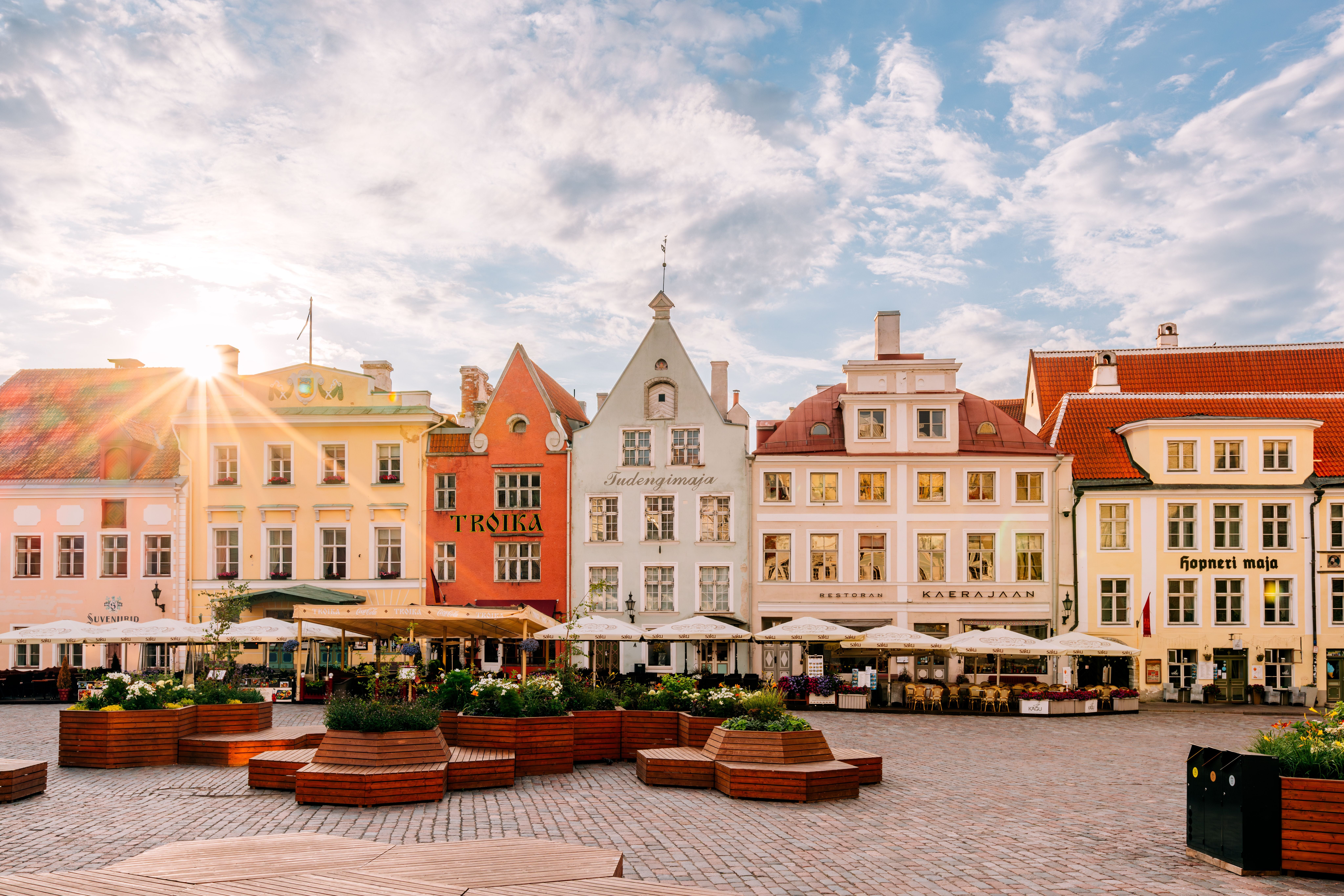 Bunte Altstadthäuser mit Cafés und Sonnenschirmen an einem sonnigen Marktplatz.