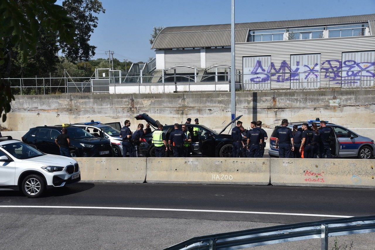 Mehrere Polizisten stehen auf einer Autobahn neben gestoppten Autos und führen eine Kontrolle durch.