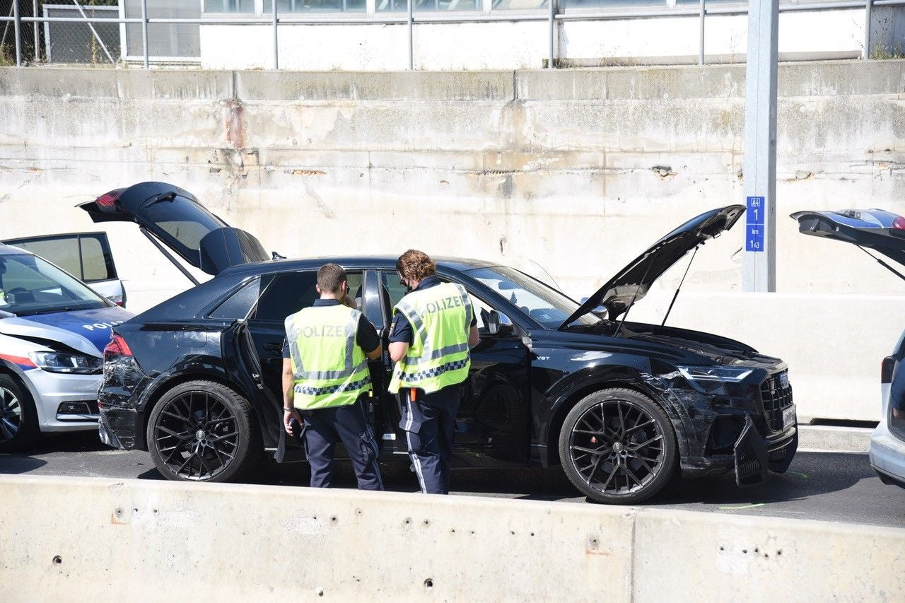 Zwei Polizisten begutachten ein beschädigtes Auto mit offener Motorhaube auf der Autobahn.