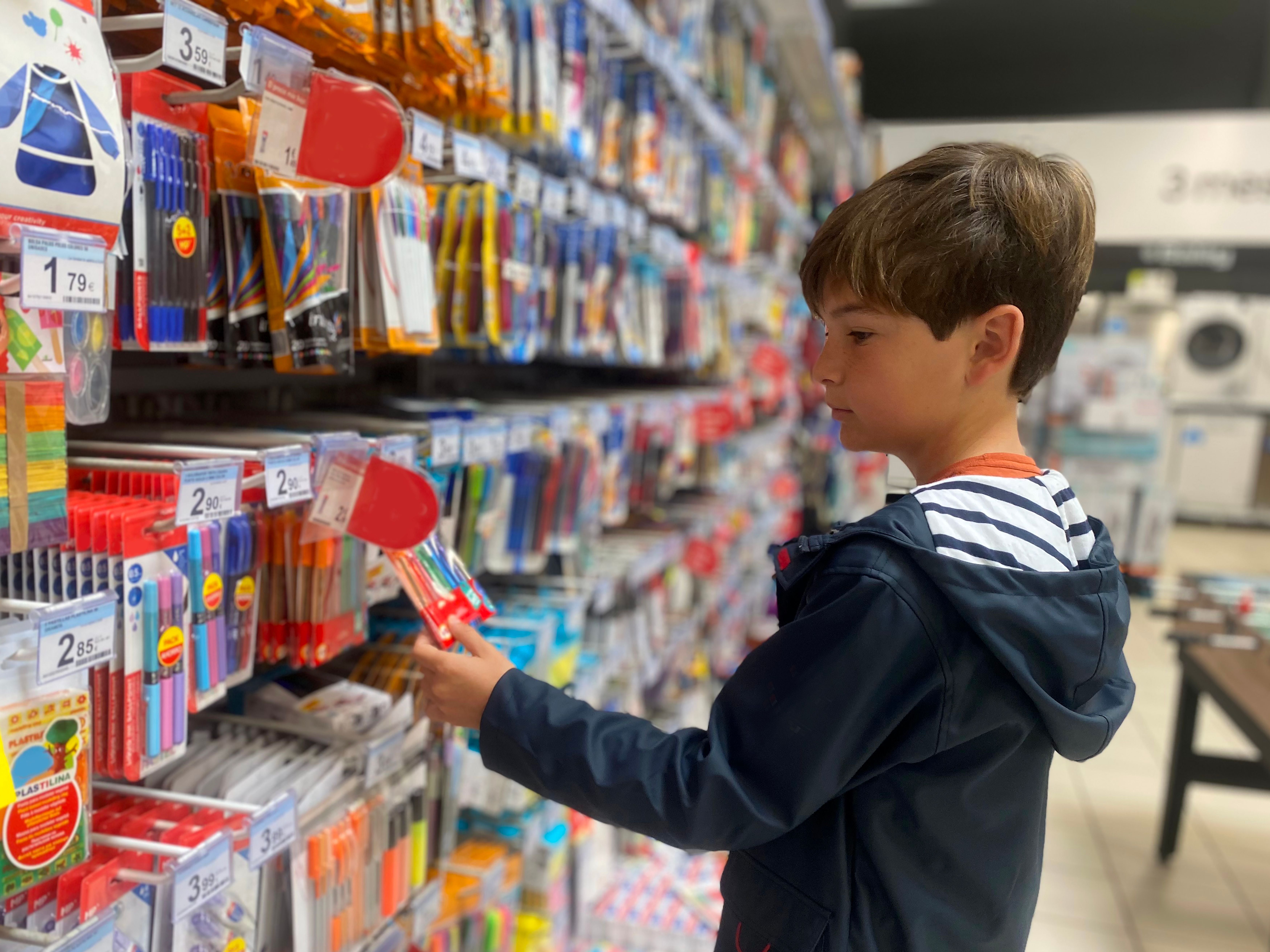 Junge sucht Schreibwaren in einem Geschäft aus dem Regal aus.