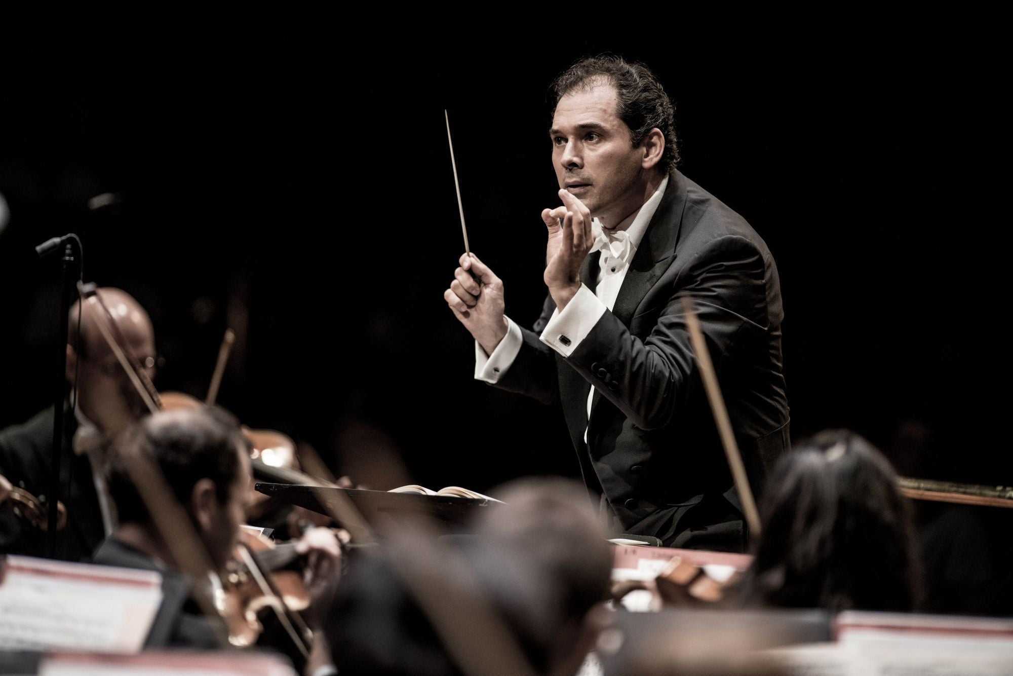 Dirigent leitet ein Orchester während eines Konzerts mit erhobenem Taktstock.