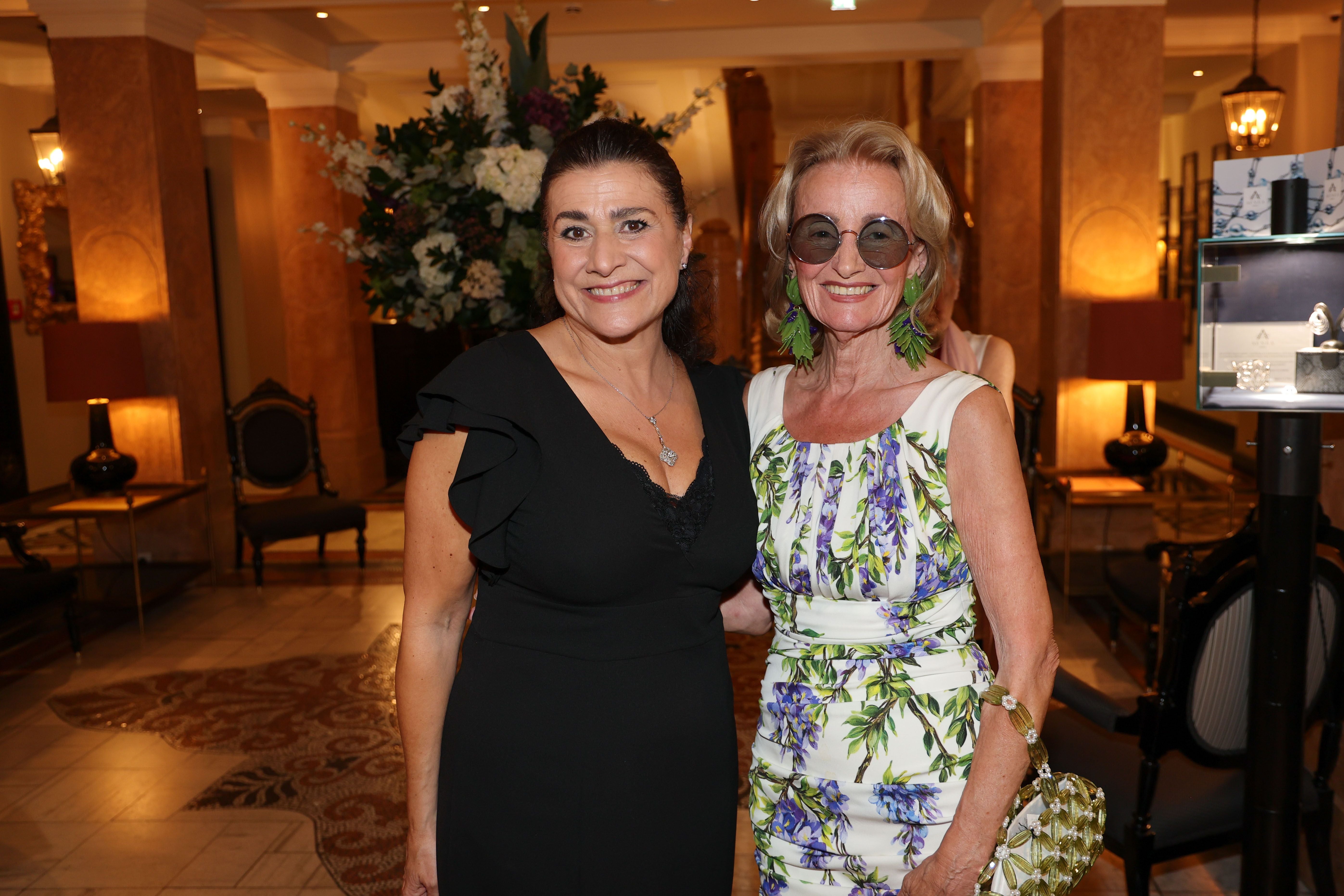 Zwei elegant gekleidete Frauen lächeln bei einer Premierenfeier im Hotel Sacher in Salzburg.