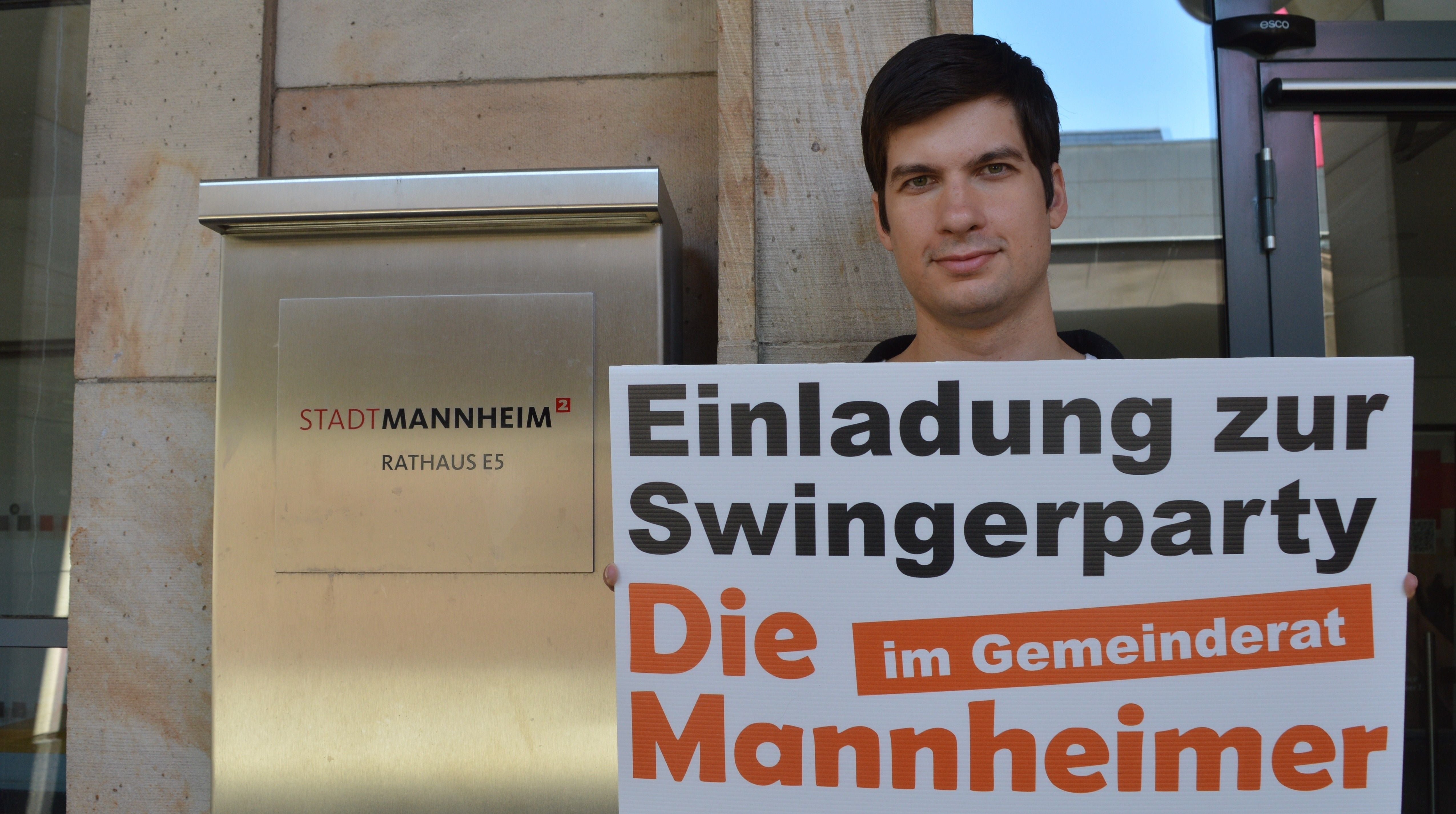 Ein Mann hält vor dem Mannheimer Rathaus ein Schild mit der Aufschrift „Einladung zur Swingerparty“.