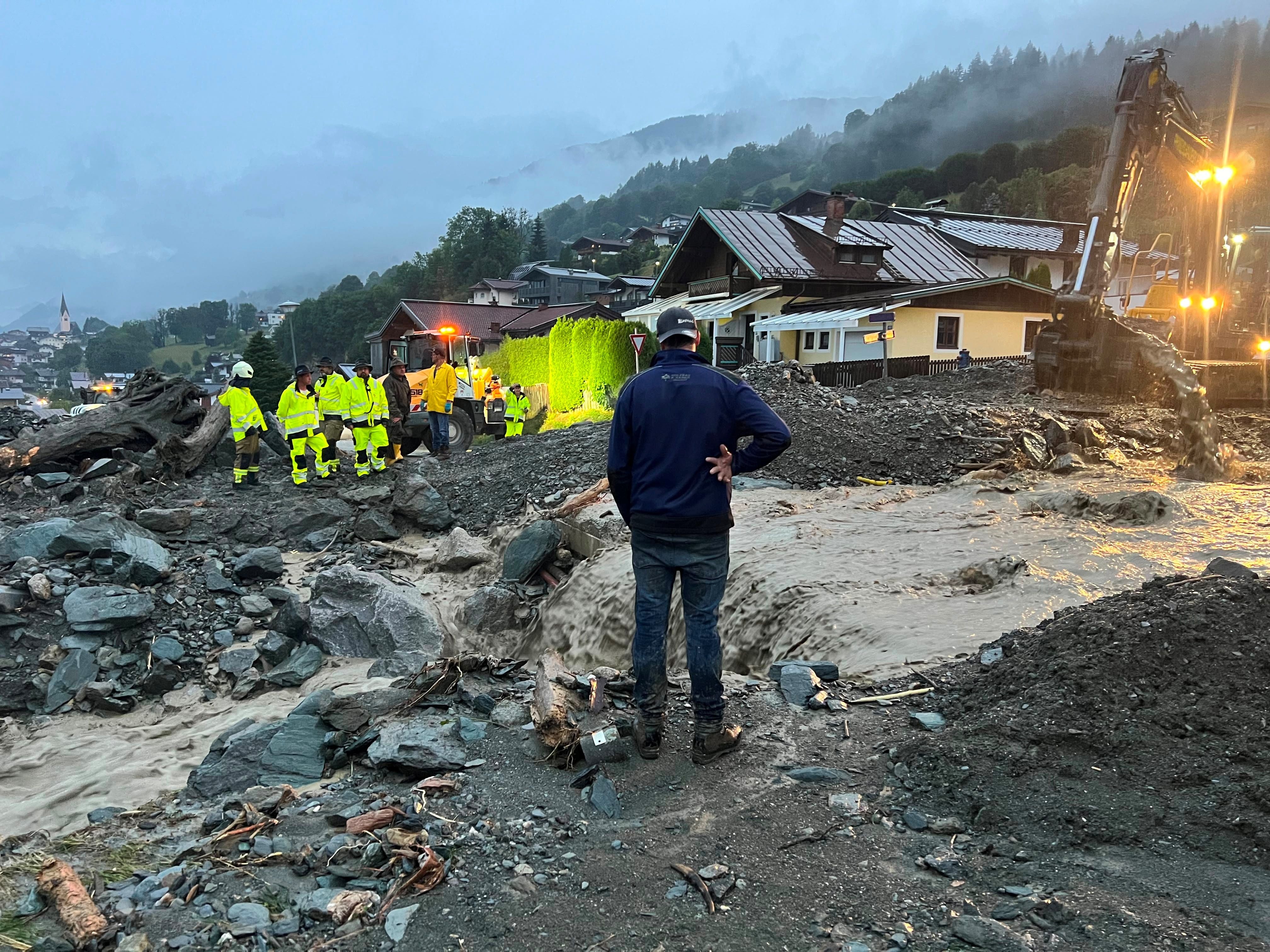 Einsatzkräfte arbeiten bei Hochwasser an überfluteter Baustelle in einem Alpenort bei Dämmerung.