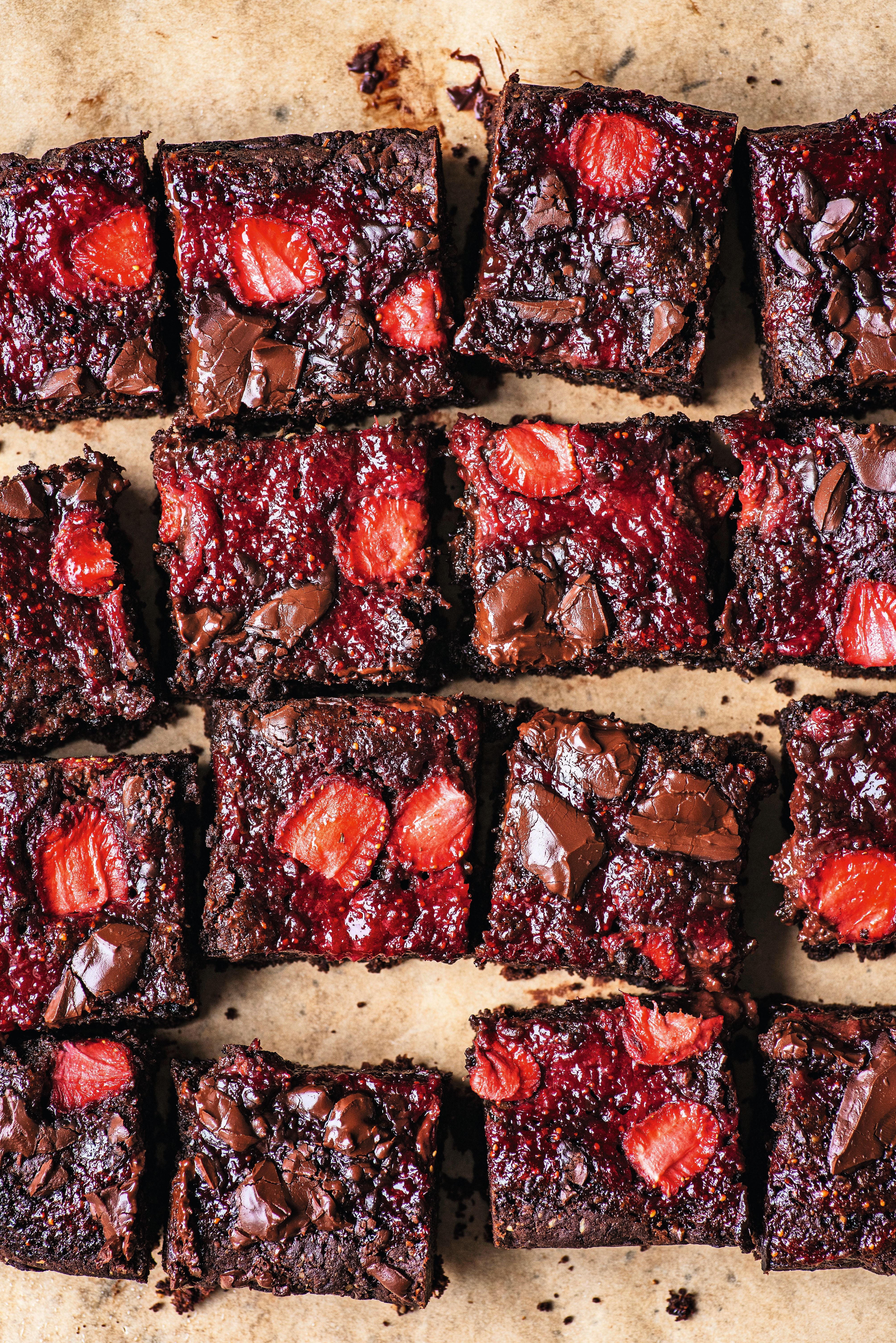 Mehrere Stücke Erdbeer-Brownies mit Schokoladenstückchen auf Backpapier.