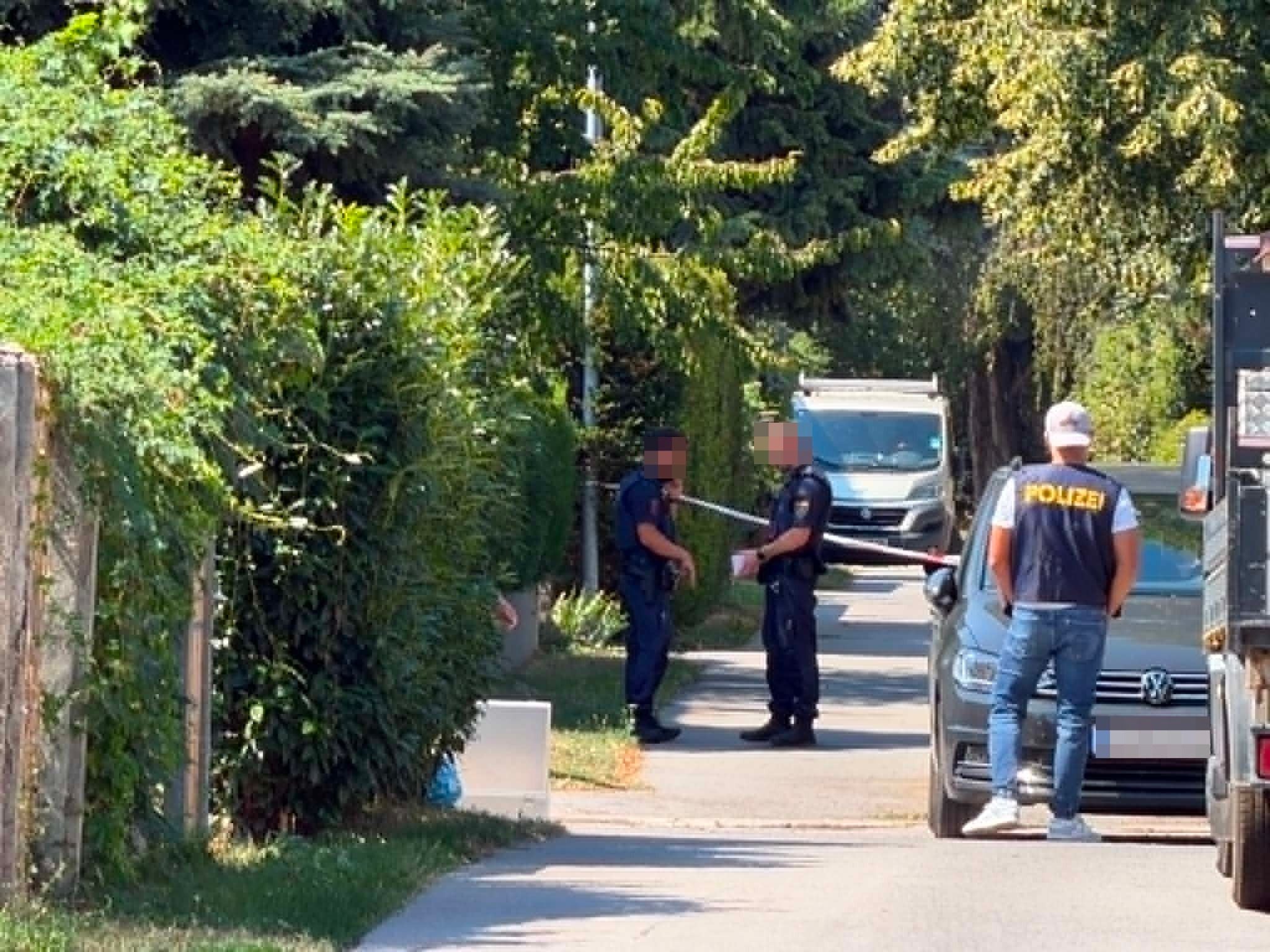 Polizisten sperren eine Straße mit Absperrband in einem Wohngebiet ab.