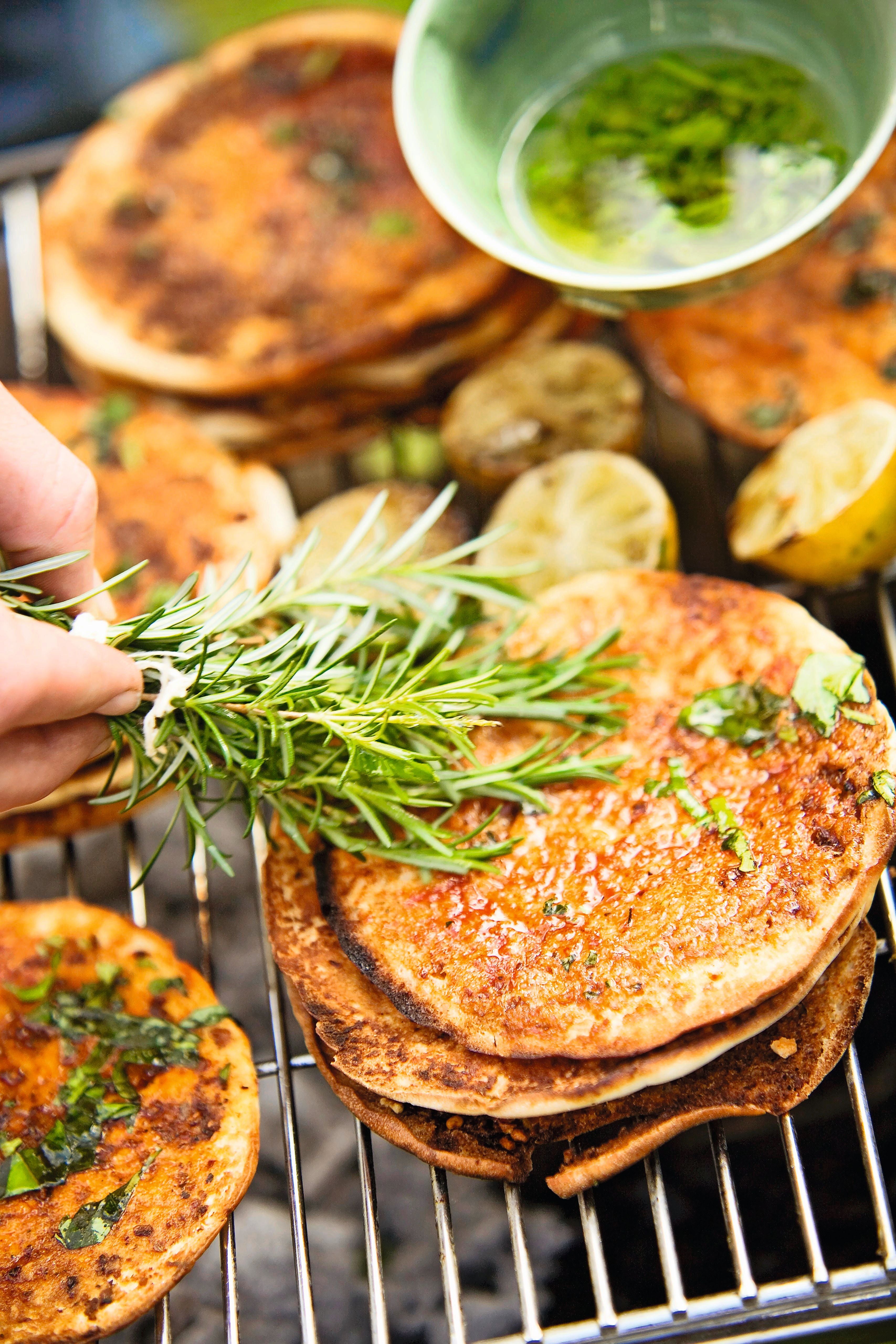 Gegrillte Pitabrote werden mit Chermoula-Basilikum-Öl und frischem Rosmarin bestrichen.