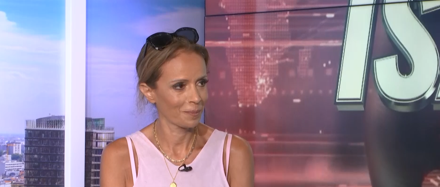 Frau mit Sonnenbrille auf dem Kopf sitzt in einem Fernsehstudio und unterhält sich.