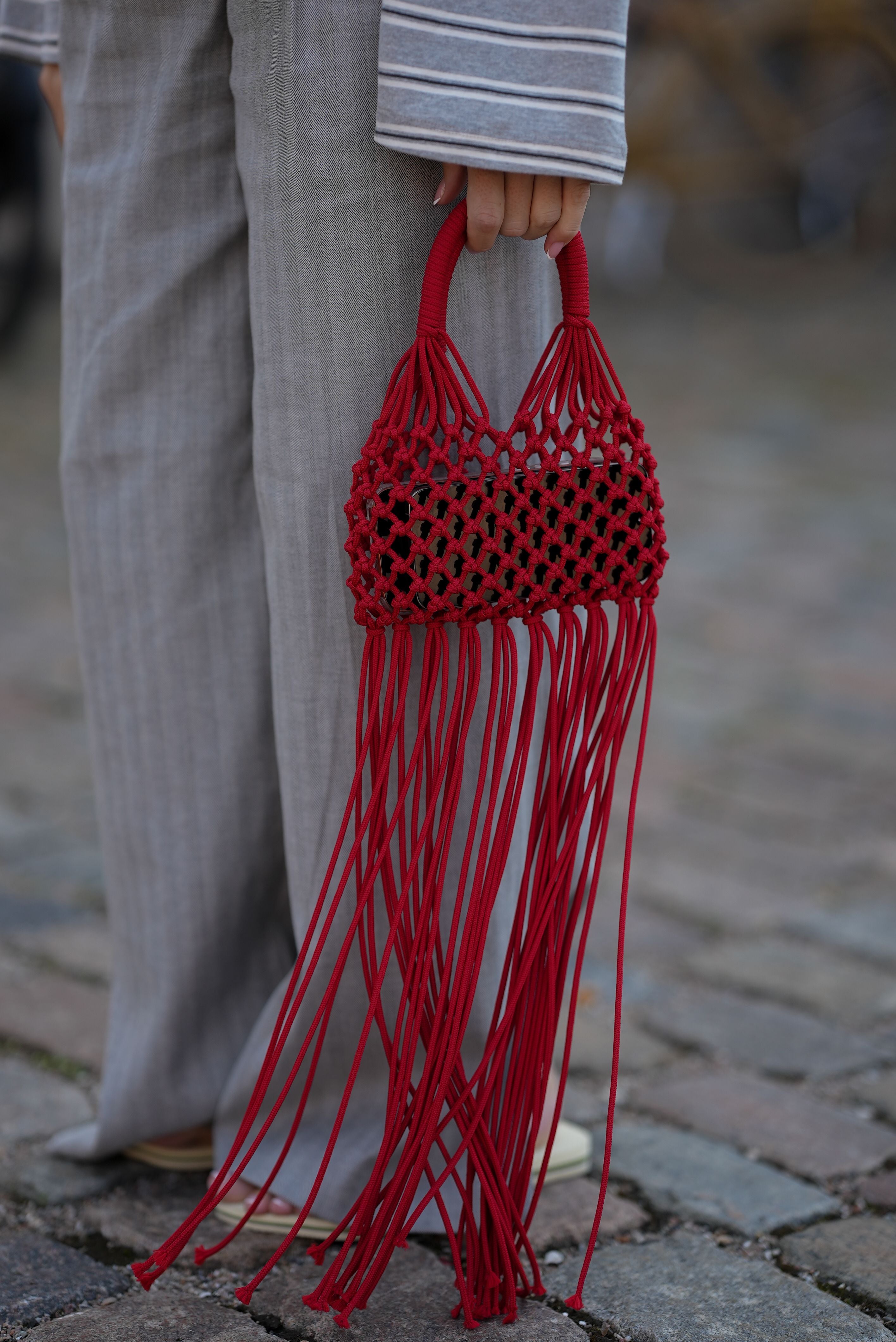Rote Statement-Fransenhandtasche wird zu grauen weiten Stoffhosen getragen.