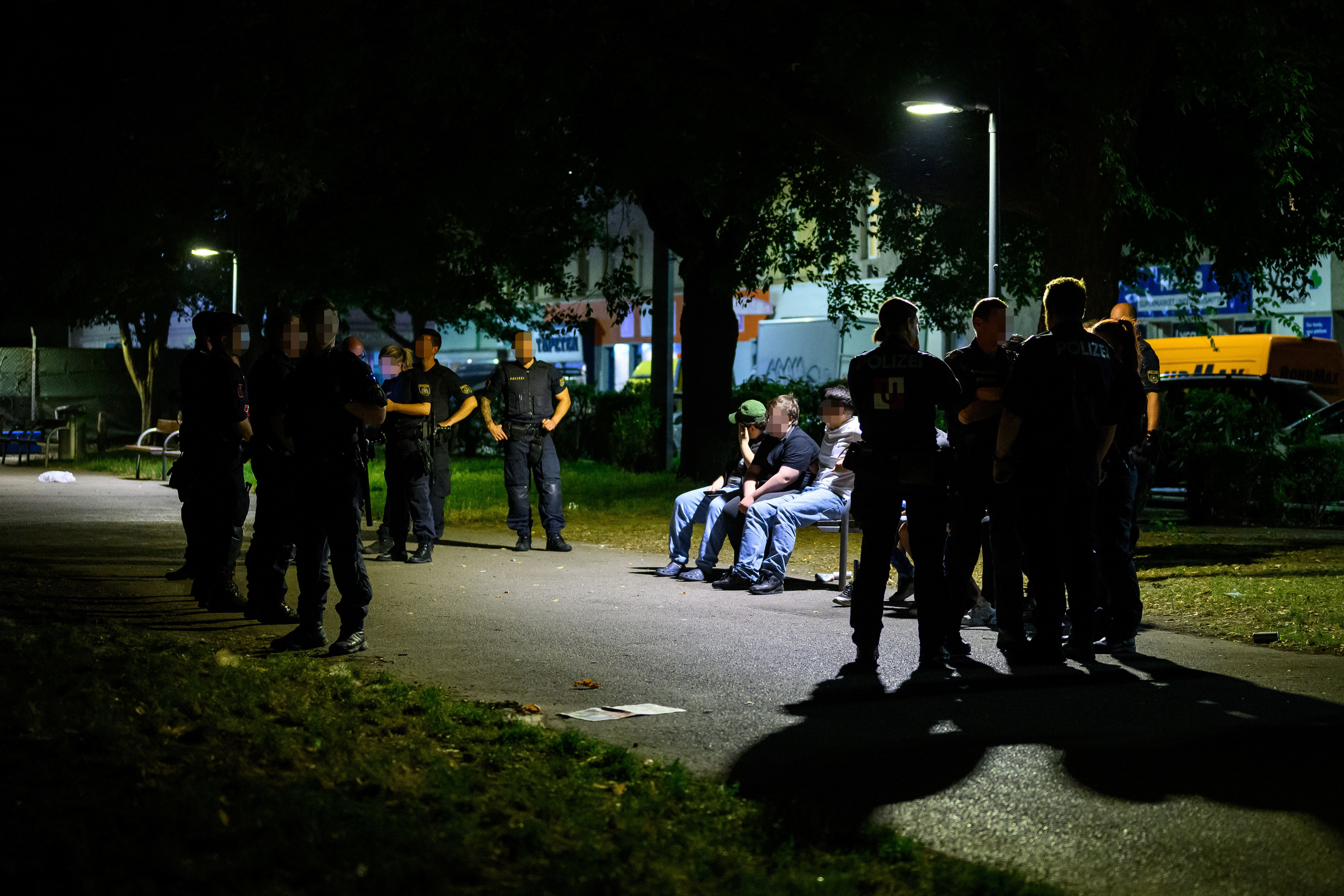 Polizisten kontrollieren bei Nacht mehrere Personen auf einer Parkbank in Wien.