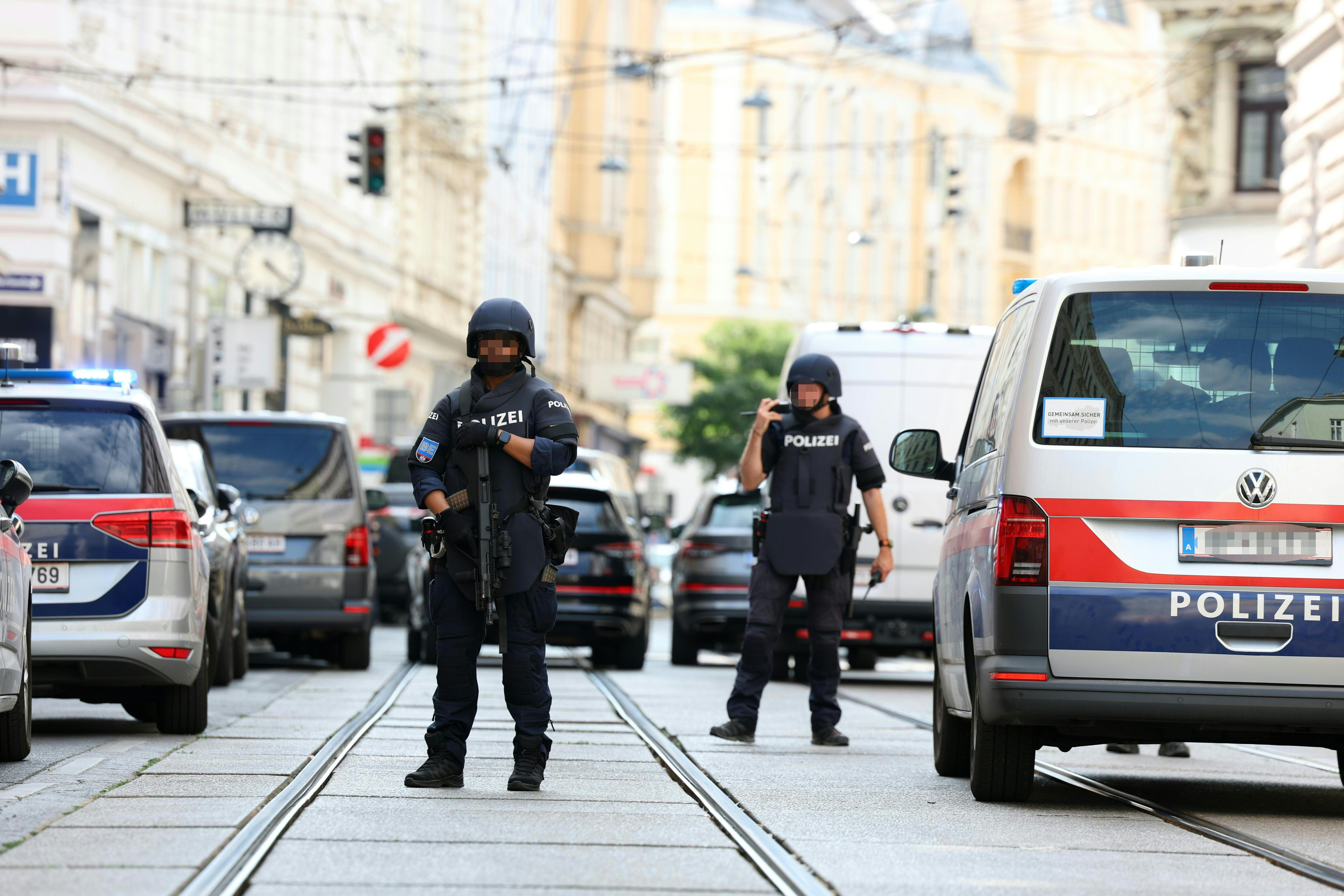 Schwer bewaffnete Polizisten stehen in Wien neben Einsatzfahrzeugen auf einer abgesperrten Straße.