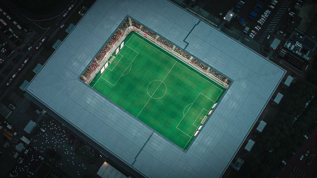 Luftaufnahme eines Fußballstadions mit grünem Spielfeld und Zuschauern auf den Tribünen.