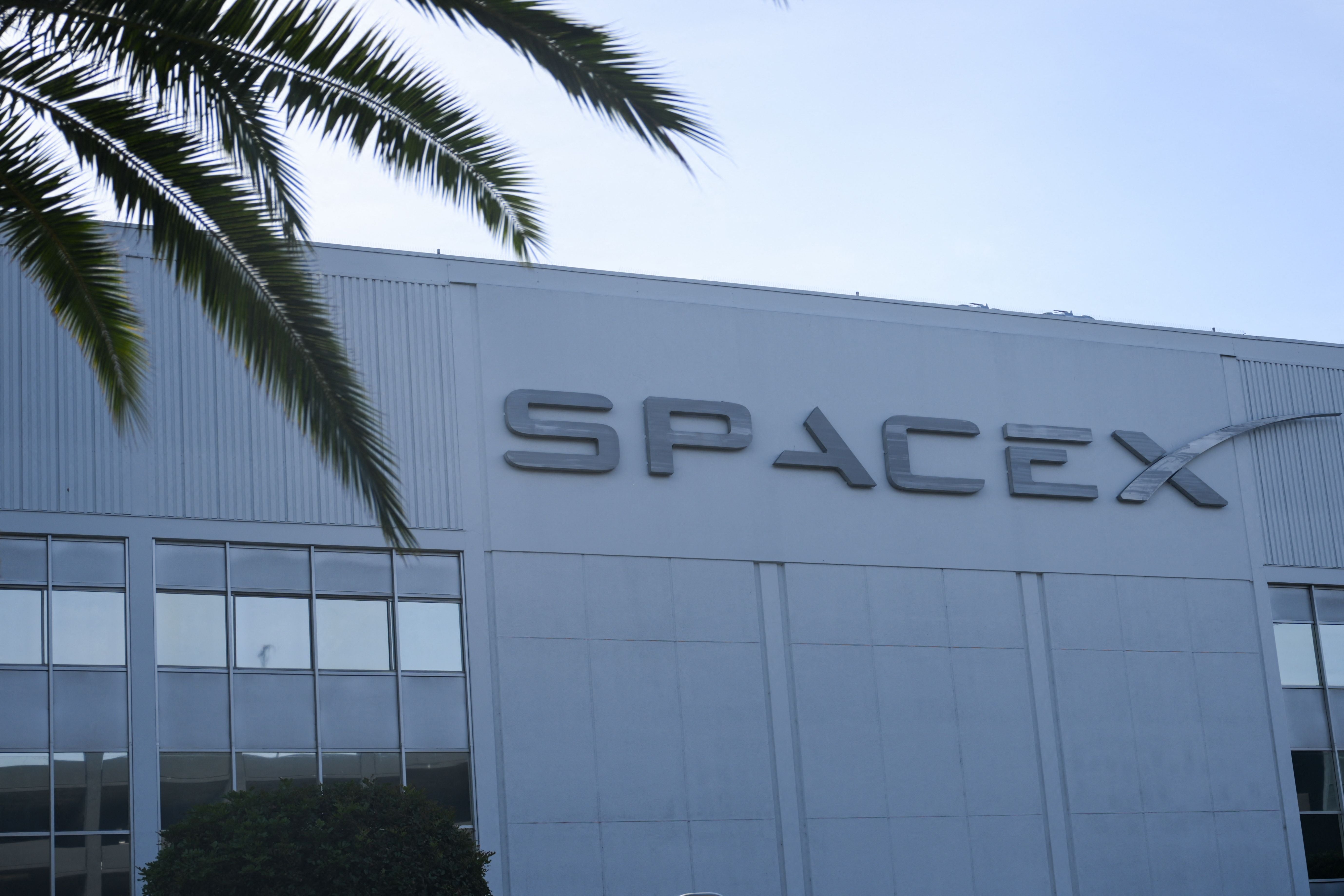Das SpaceX-Logo ist an einem Gebäude mit Fenstern und Palmen im Vordergrund angebracht.