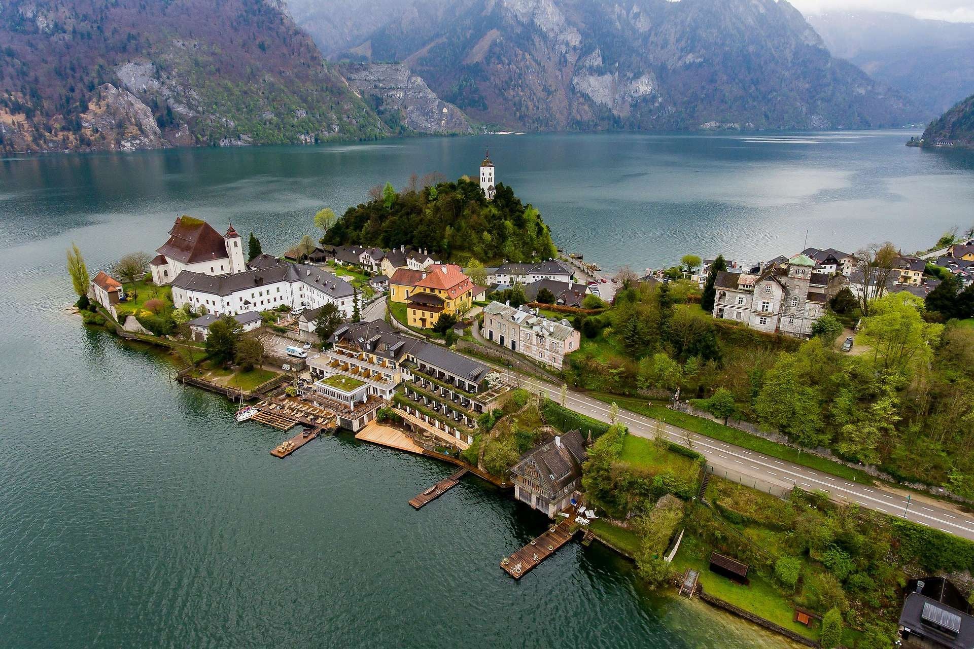 Luftaufnahme einer kleinen österreichischen Ortschaft am See mit Bergen im Hintergrund.
