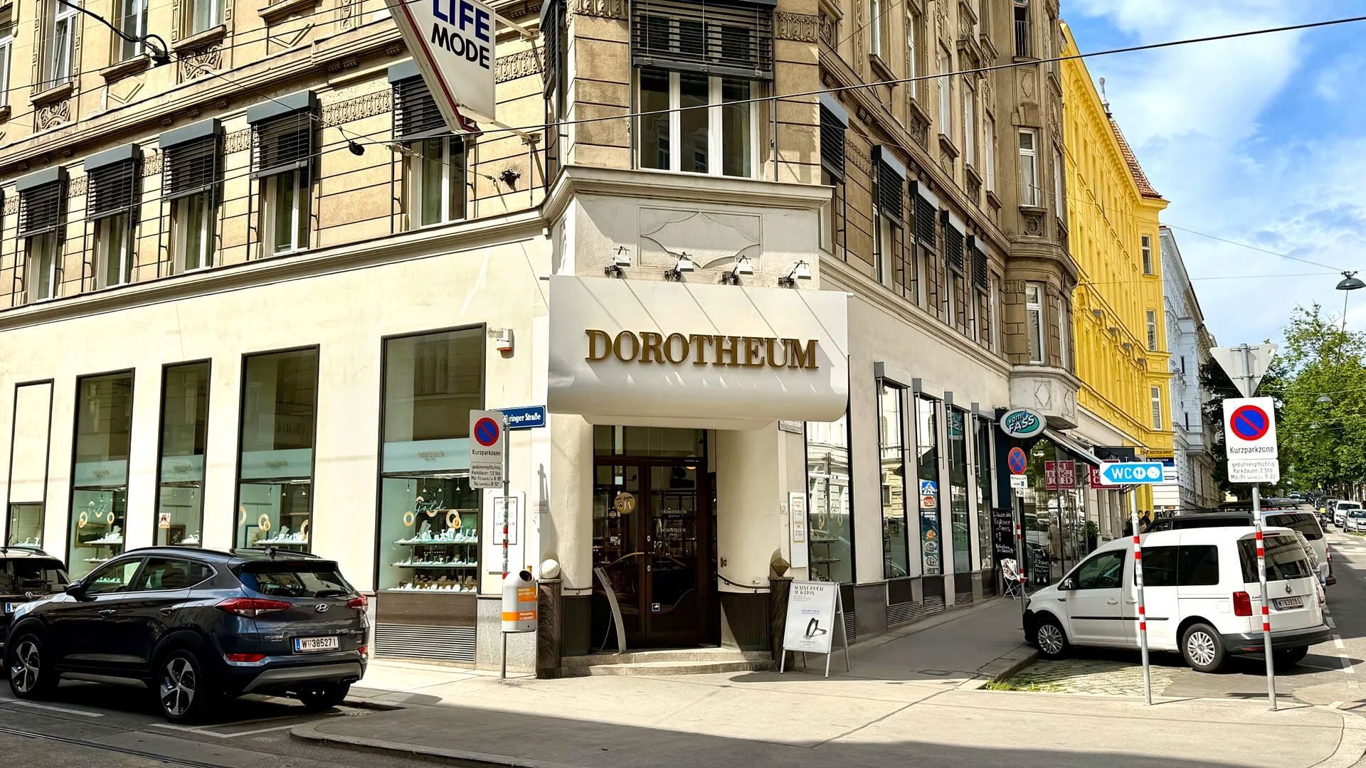 Eingang des Dorotheum an der Währinger Straße mit Schaufenstern und geparkten Autos.