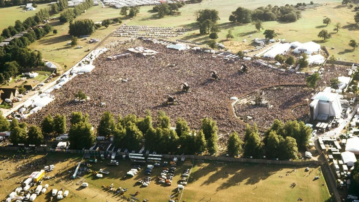 Luftaufnahme eines riesigen Open-Air-Konzerts mit tausenden Menschen auf einer Wiese.