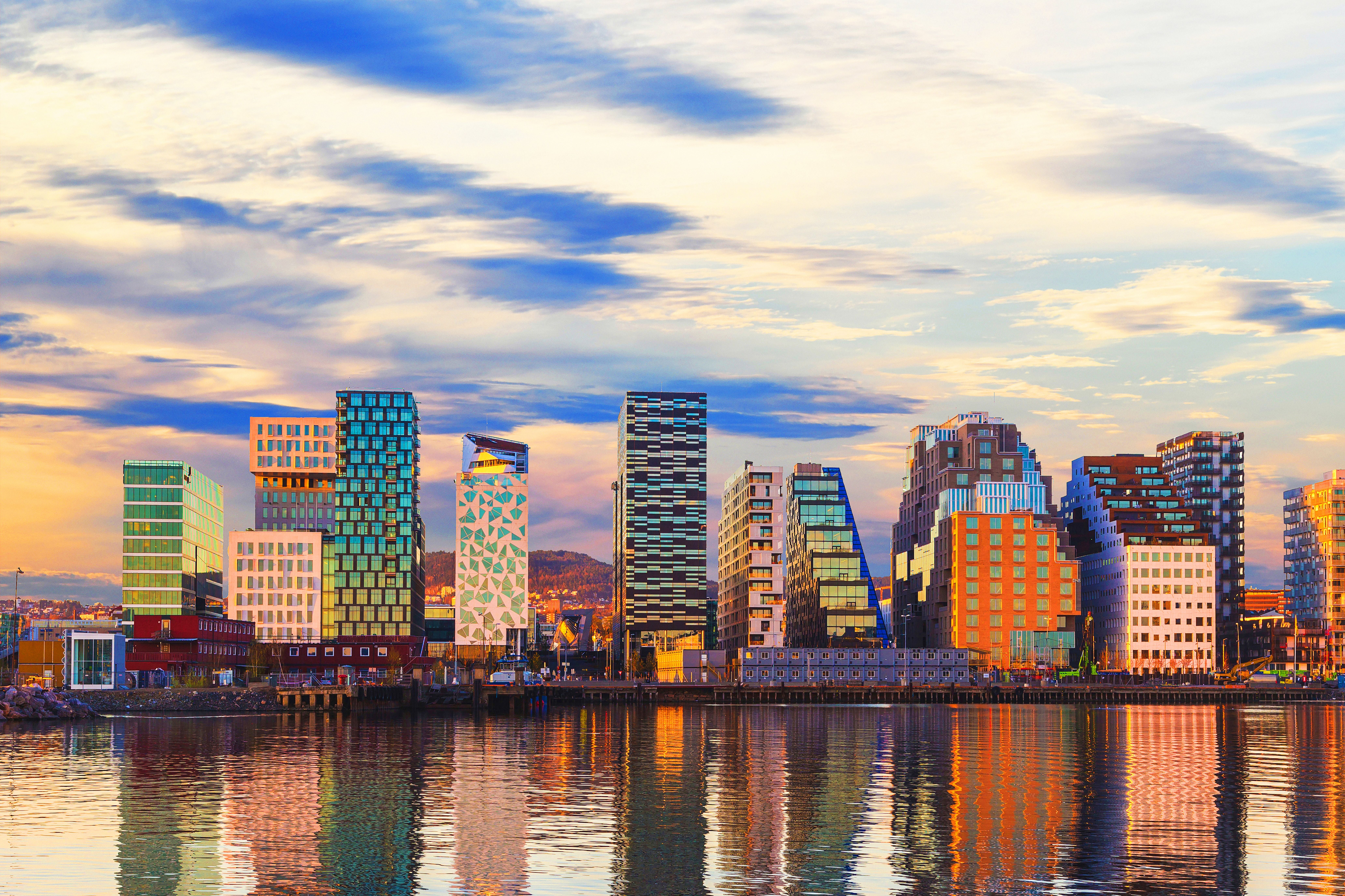 Moderne Hochhäuser am Wasser in Oslo bei Sonnenuntergang, mit Wolken und Spiegelung im Wasser.