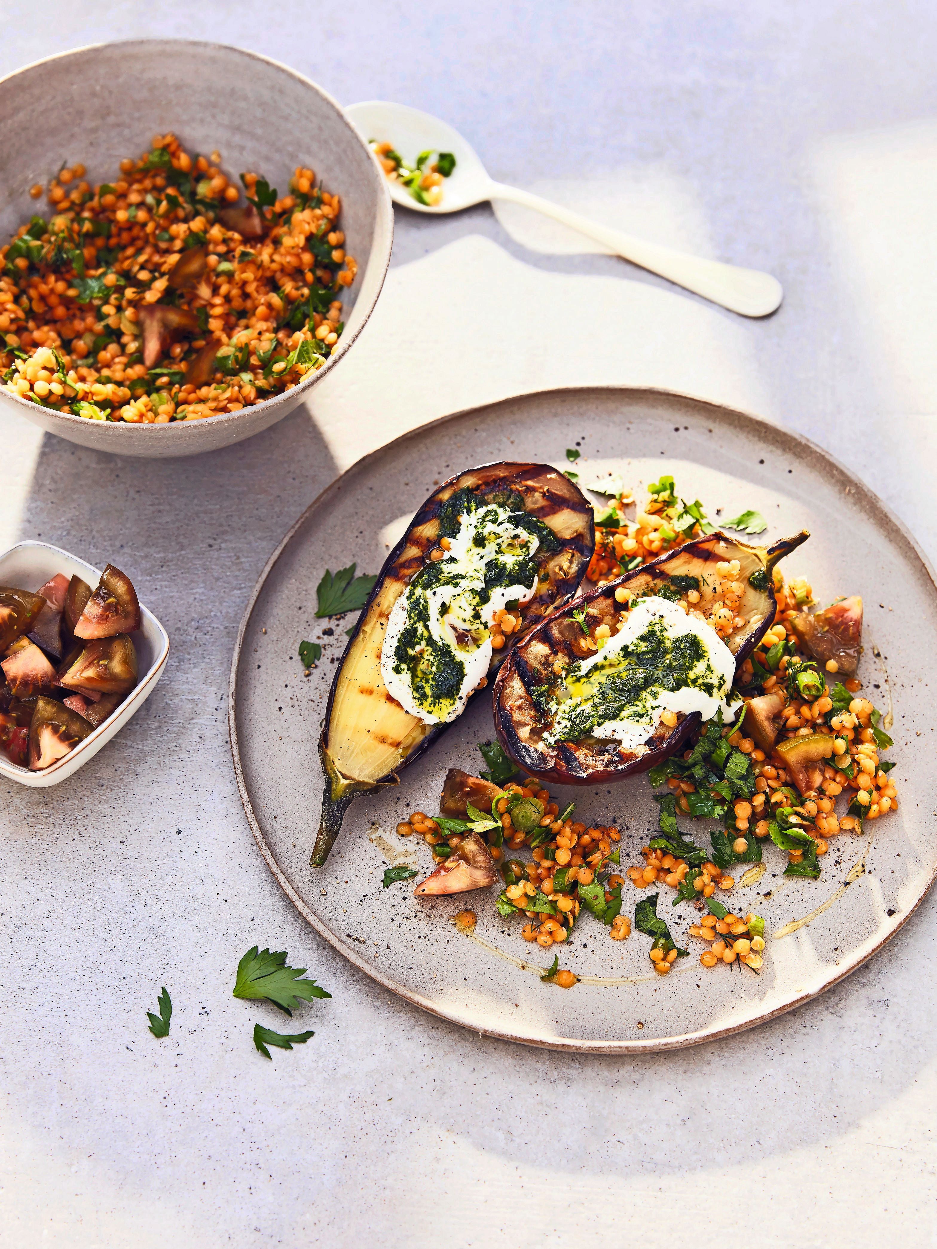 Ein Teller mit gegrillter Aubergine, roten Linsen, Joghurt und Pesto, daneben Beilagen.