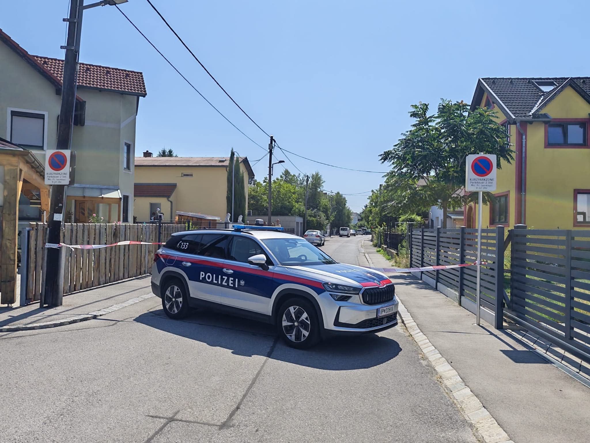 Ein österreichisches Polizeiauto sperrt eine Wohnstraße mit Absperrband ab.