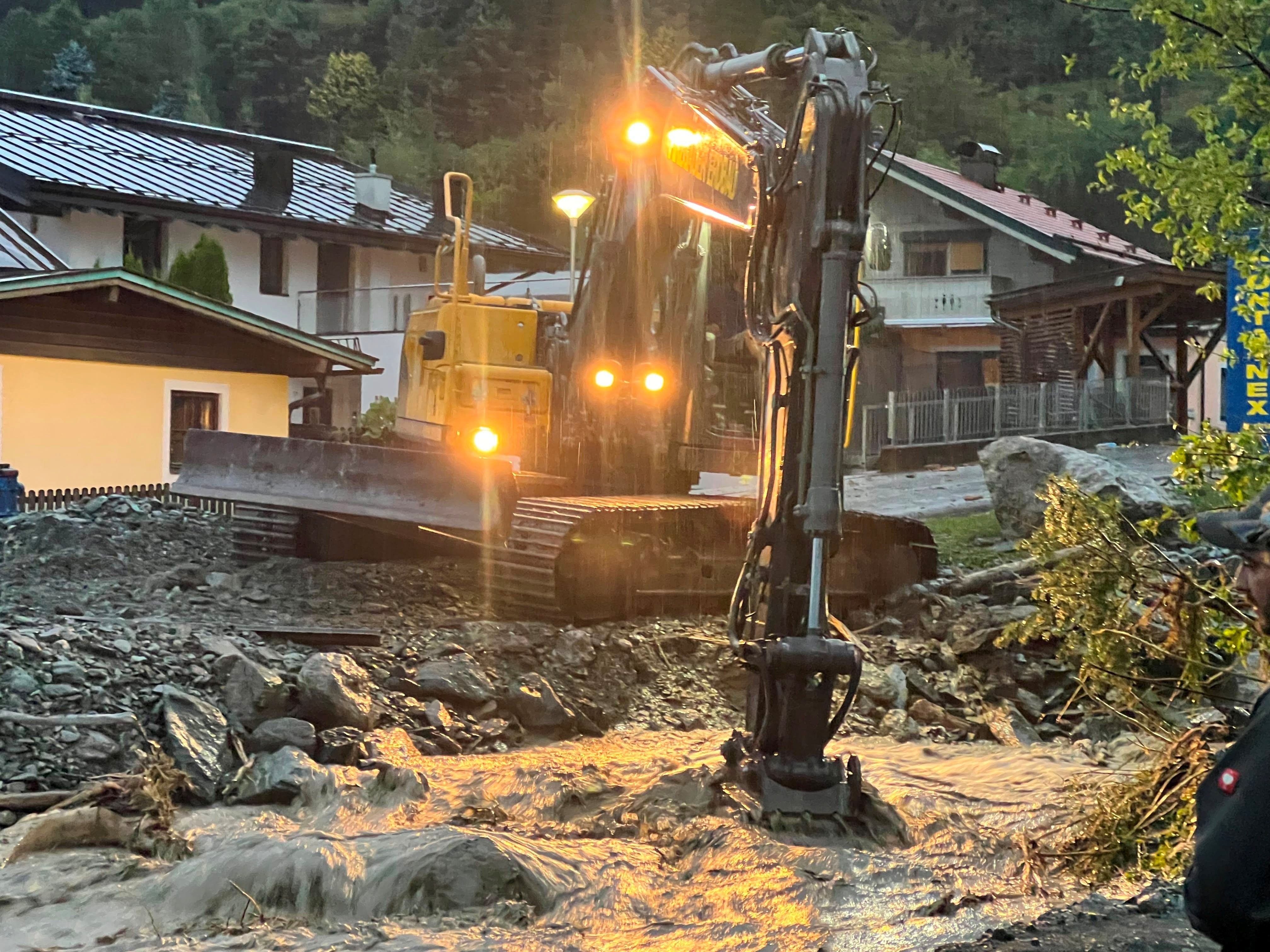 Bagger arbeitet bei Hochwasser im Bachlauf in einem Wohngebiet bei Dämmerung.
