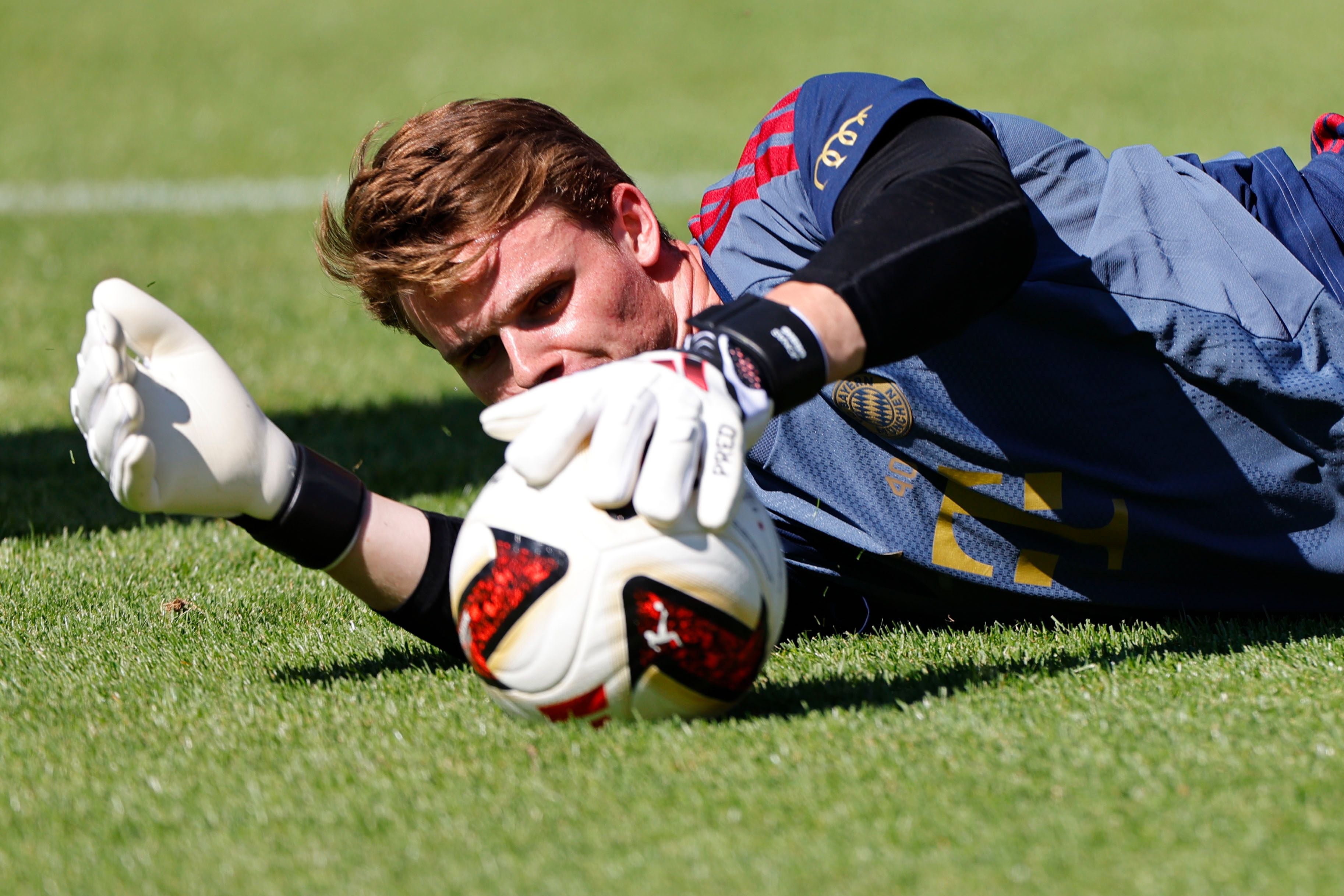 Ein Torwart mit Handschuhen hält einen Fußball beim Training auf dem Rasen fest.