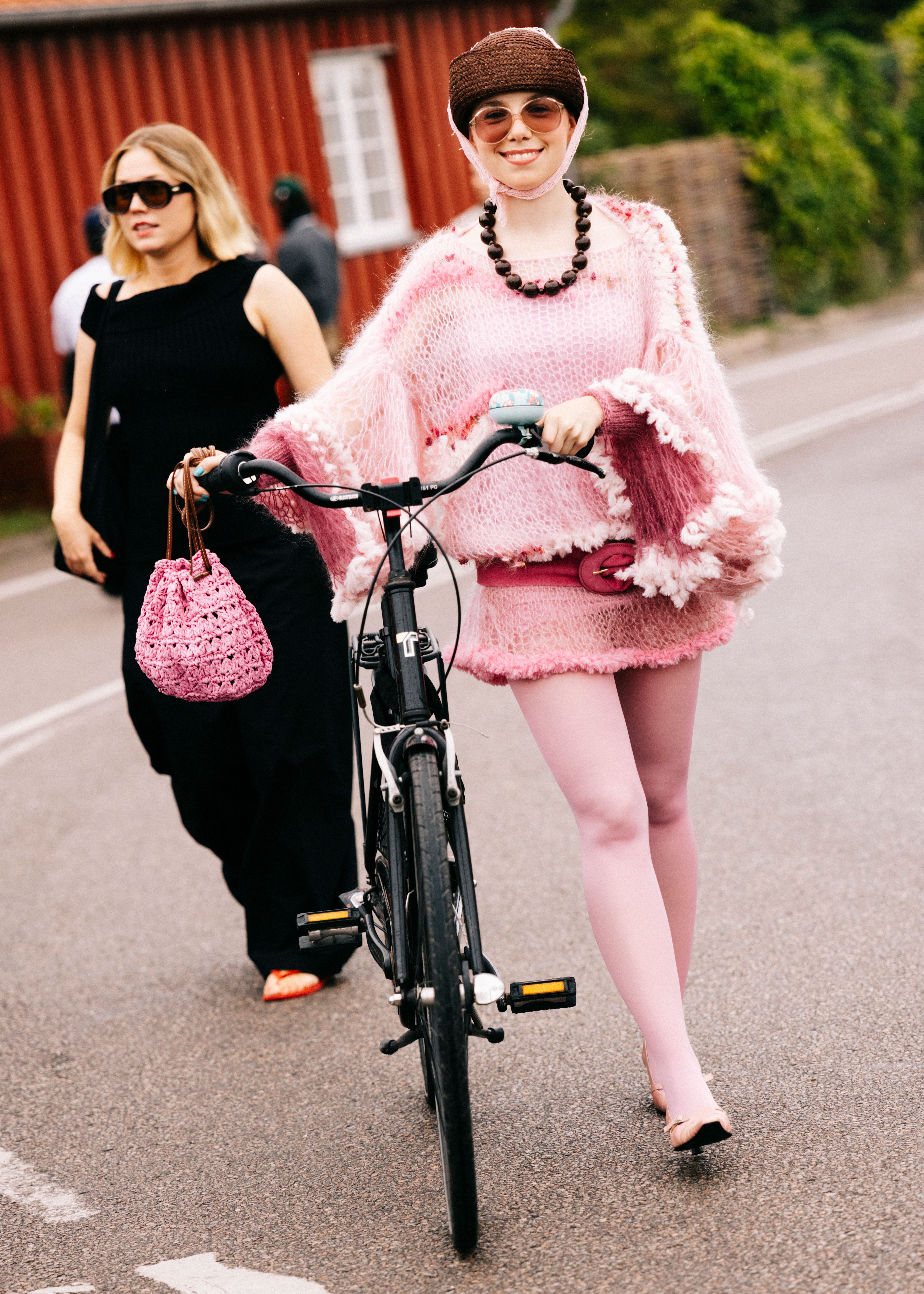 Frau in pinkem Outfit schiebt ein Fahrrad auf der Straße bei der Copenhagen Fashion Week.