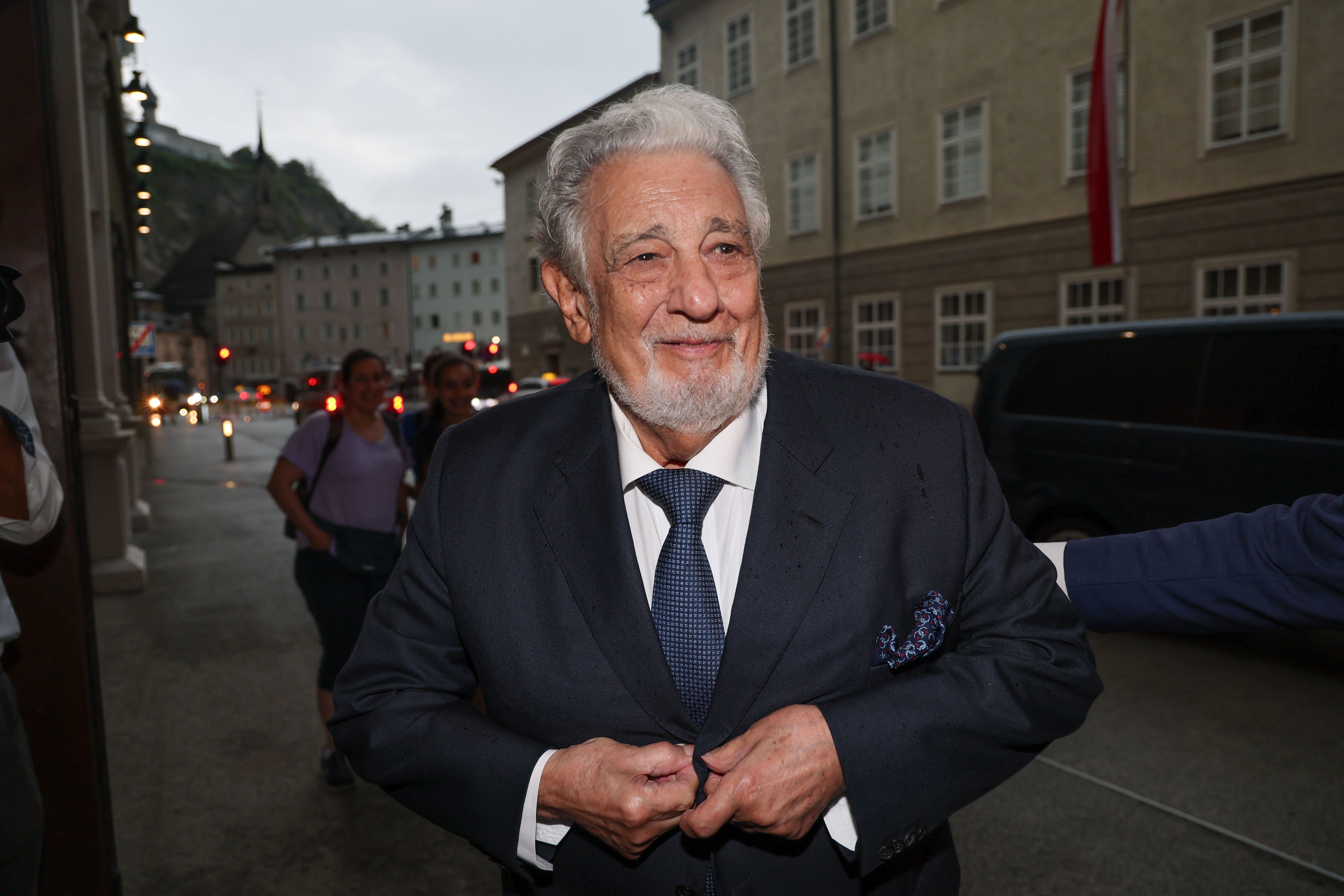 Ein älterer Mann im Anzug lächelt und knöpft seine Jacke auf einer Straße in Salzburg zu.