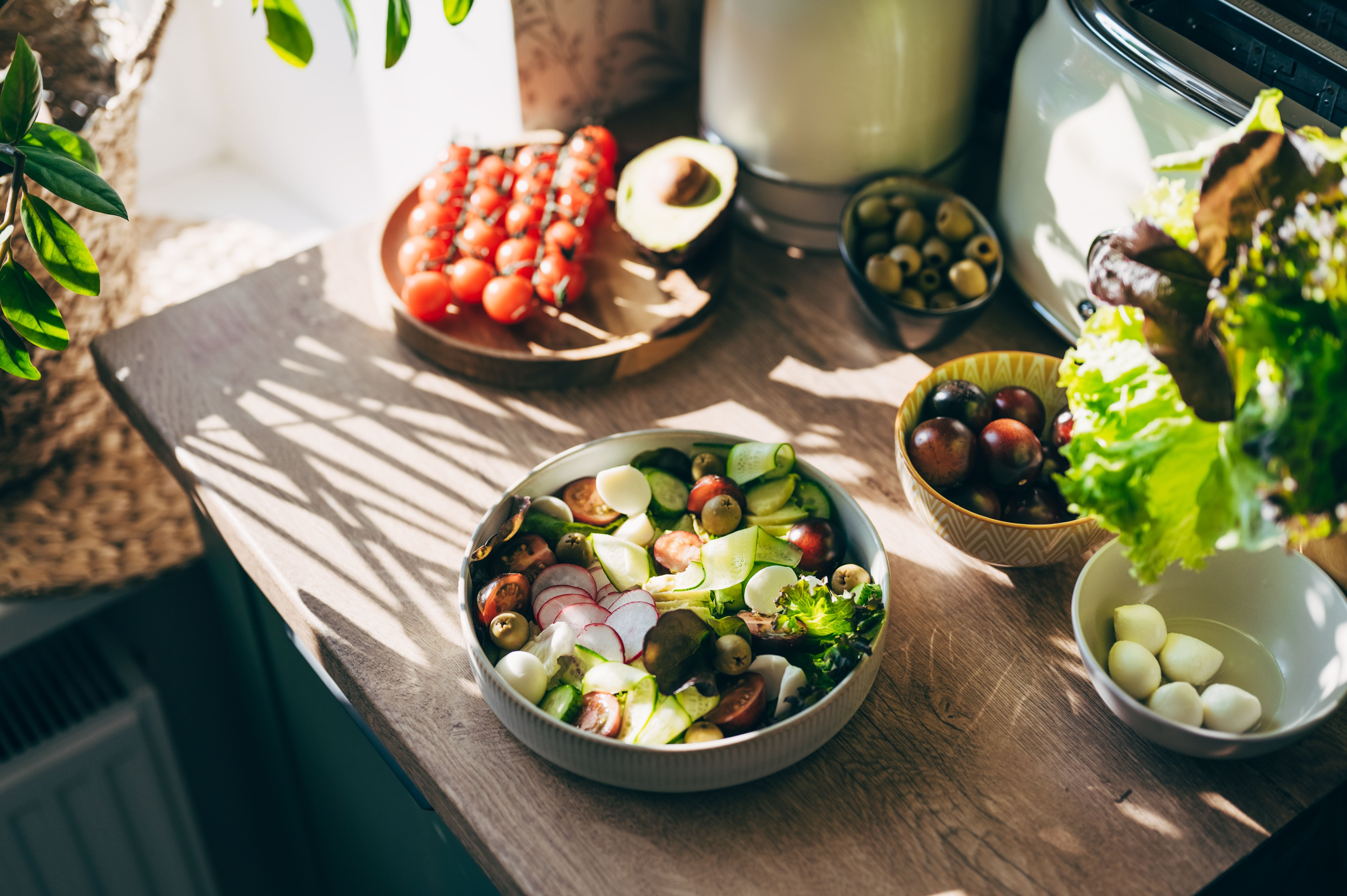 Frischer Gemüsesalat mit Tomaten, Gurken, Radieschen und Oliven auf einer sonnigen Küchenarbeitsplatte.