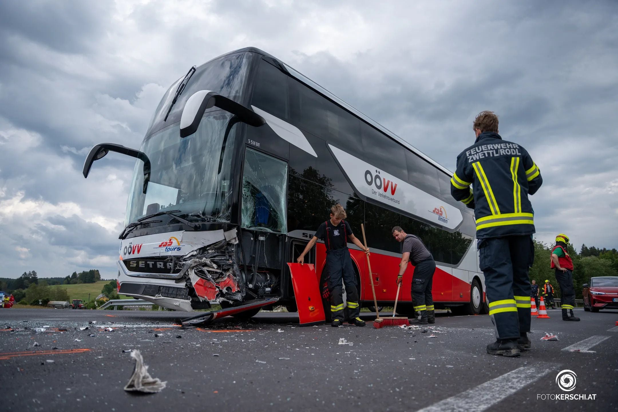 Ein beschädigter Reisebus, Feuerwehrleute räumen Trümmer nach einem Unfall auf der Straße weg.