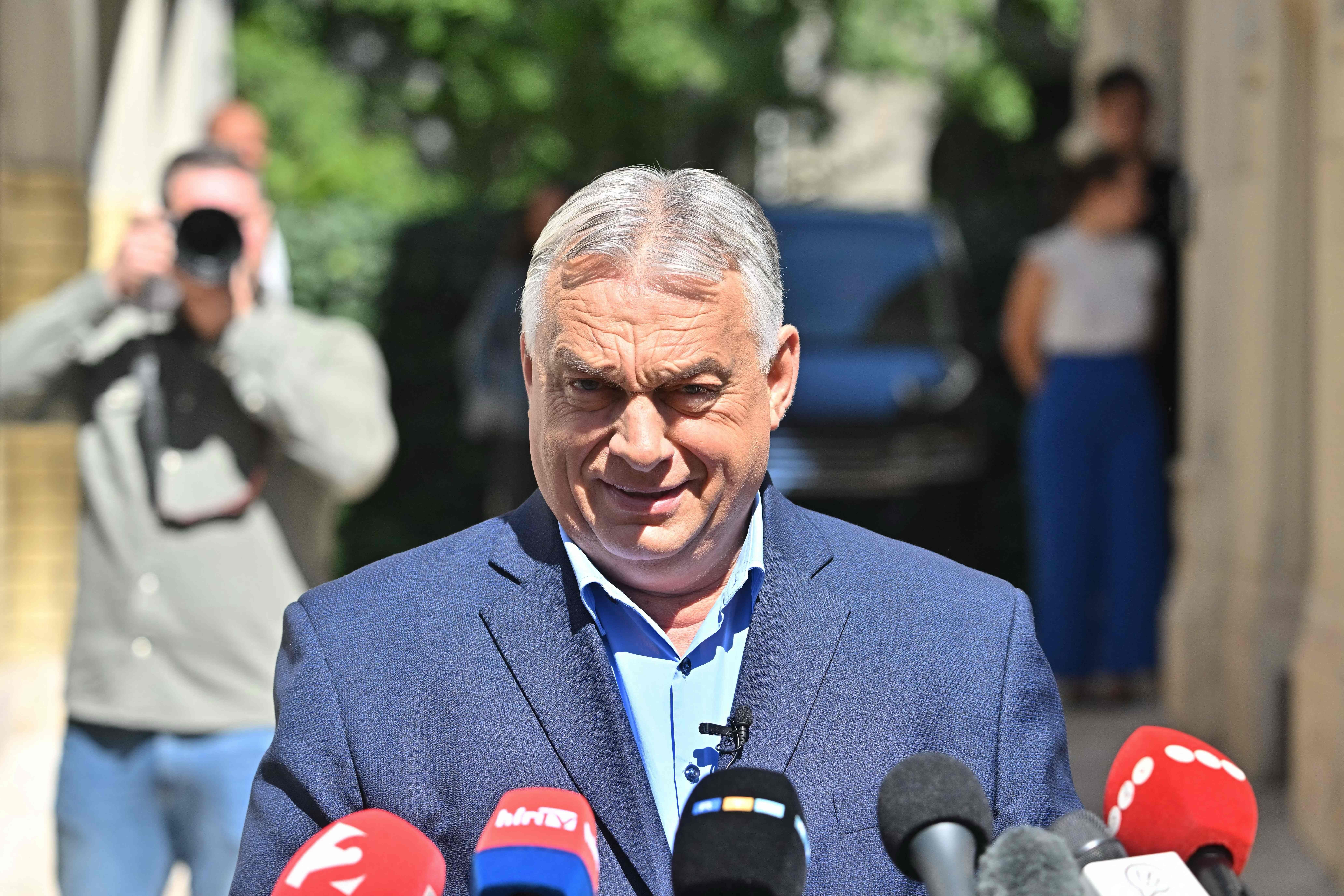 Ein Mann im Anzug spricht bei einer Pressekonferenz vor mehreren Mikrofonen im Freien.