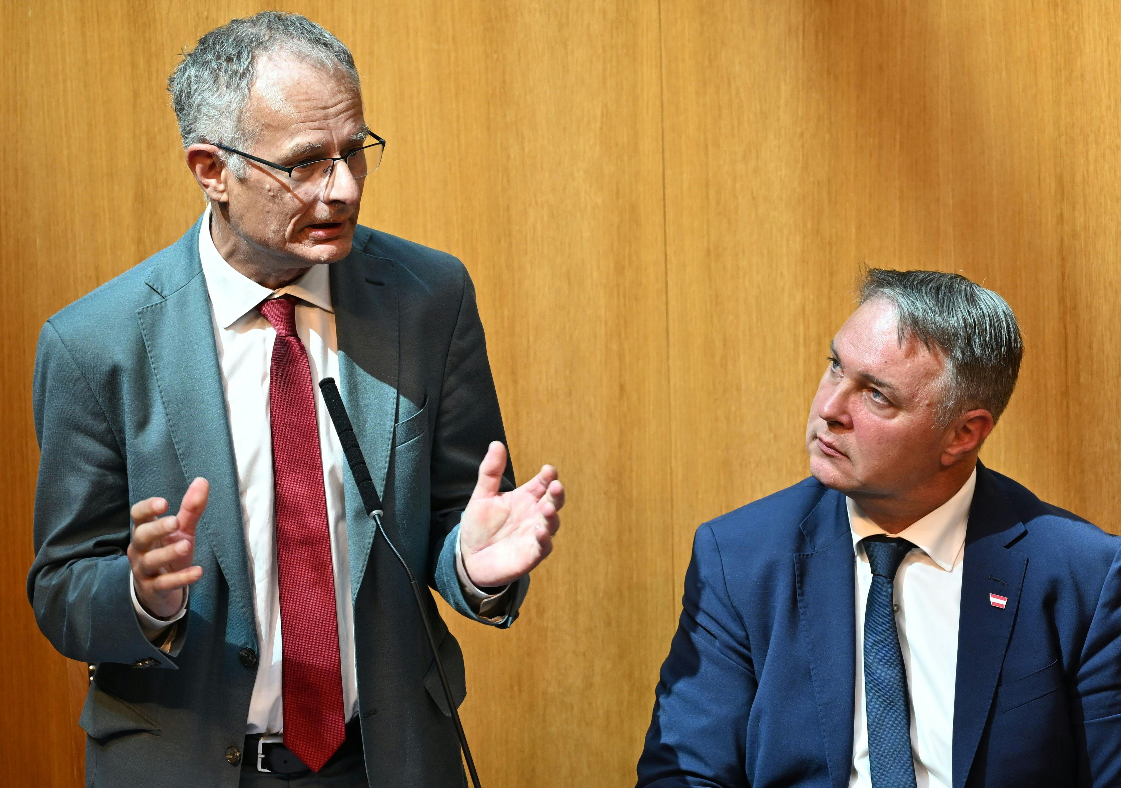 Zwei Männer im Anzug sprechen in einem holzgetäfelten Raum, einer steht am Mikrofon.