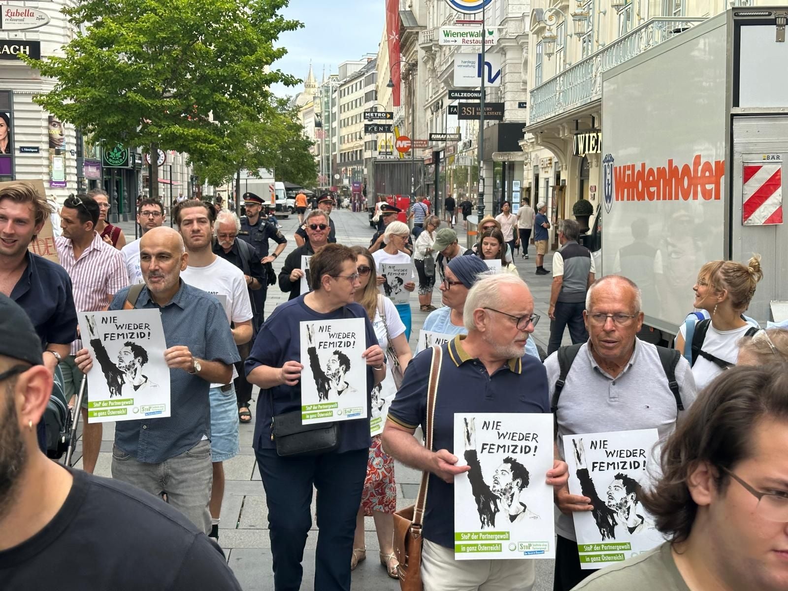 Menschen demonstrieren in einer Stadt und halten Schilder mit der Aufschrift „Nie wieder Femizid!“