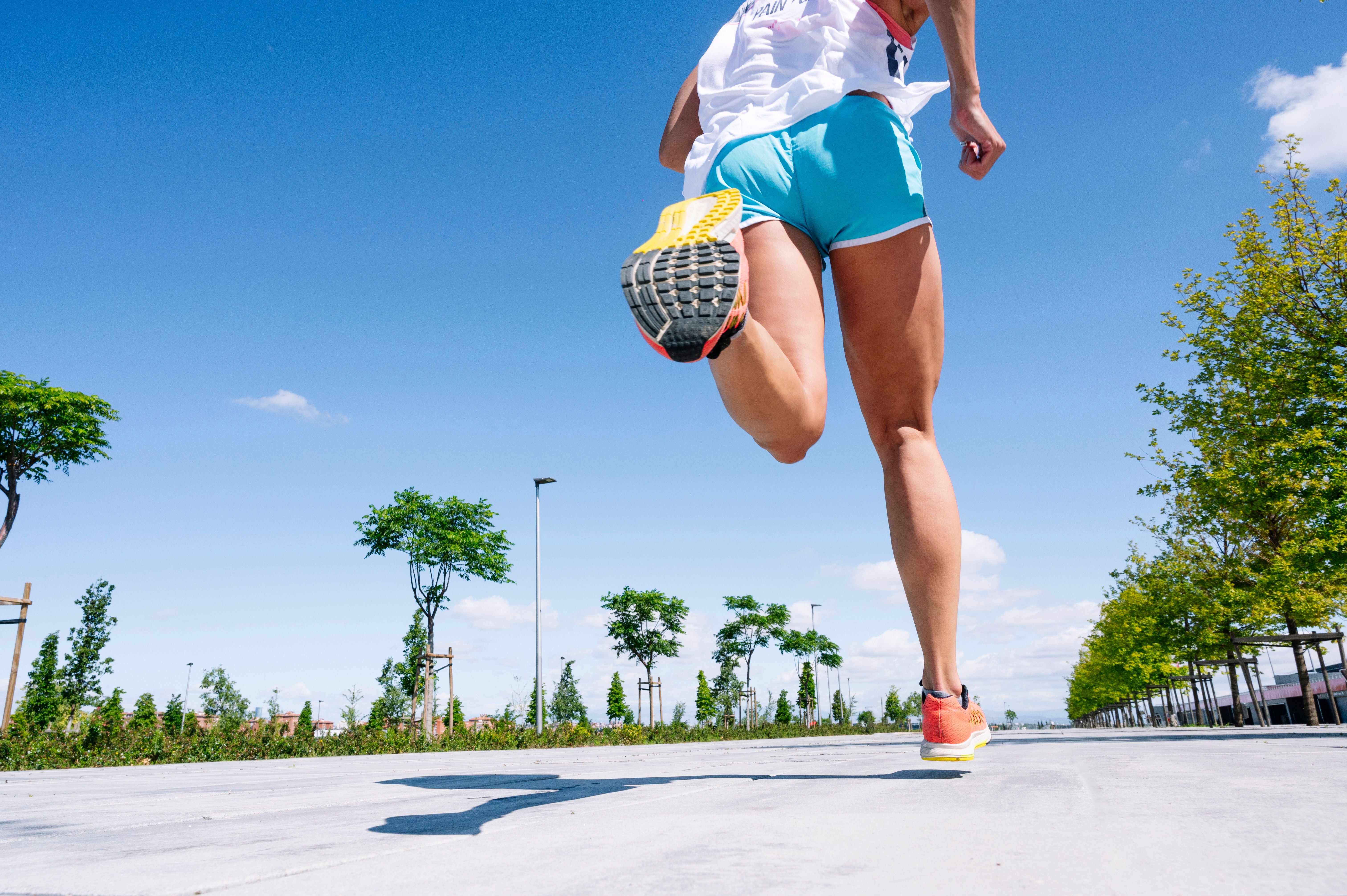 Läuferin in Sportkleidung joggt auf einem sonnigen Gehweg, aufgenommen von unten.