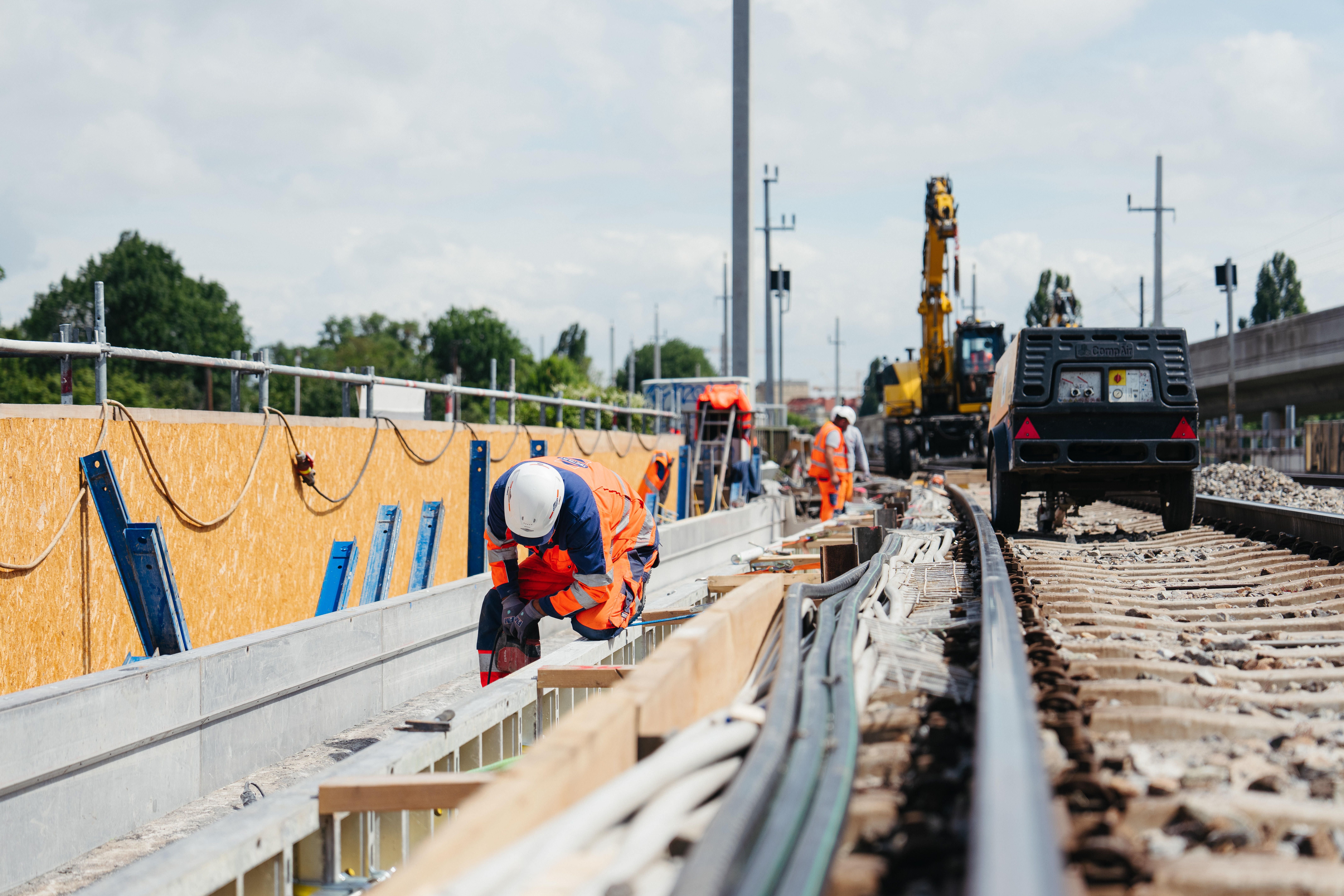 Bauarbeiter arbeiten an Gleisen einer Bahnstrecke, Maschinen und Material im Hintergrund.