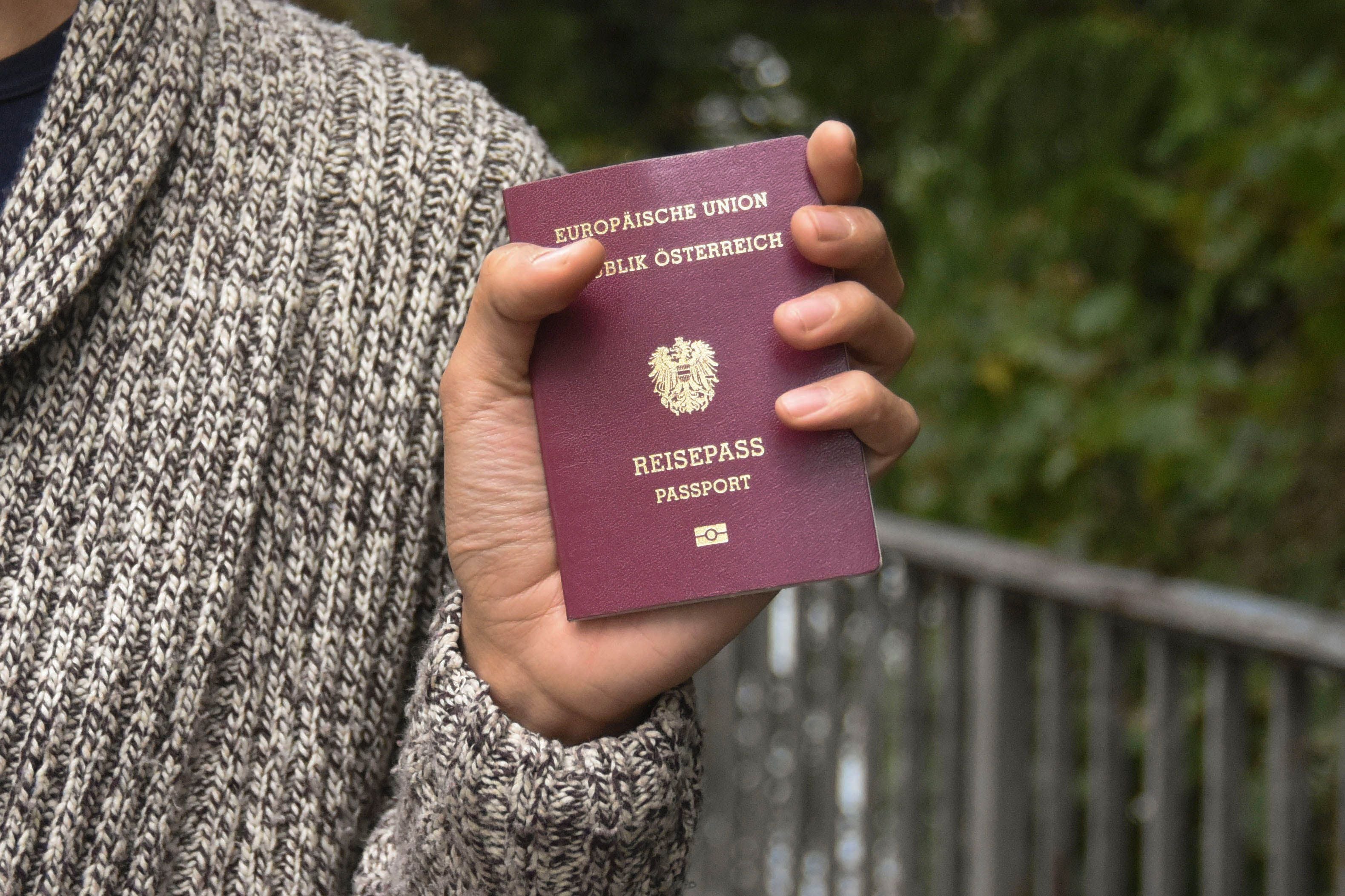 Eine Hand hält einen österreichischen Reisepass vor unscharfem Hintergrund.