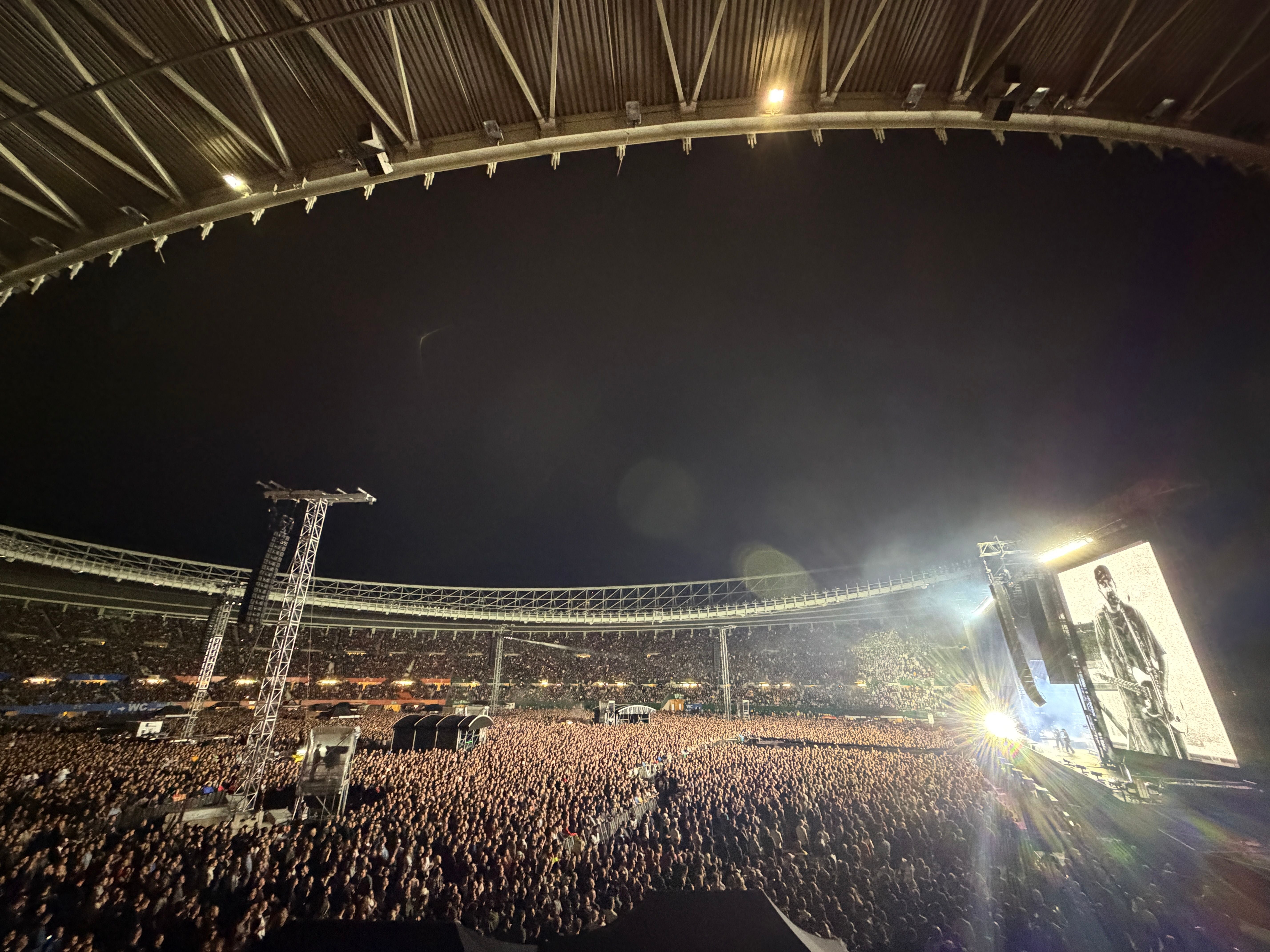 Großes Open-Air-Konzert bei Nacht, Bühne mit Videowand und riesige Menschenmenge im Stadion.