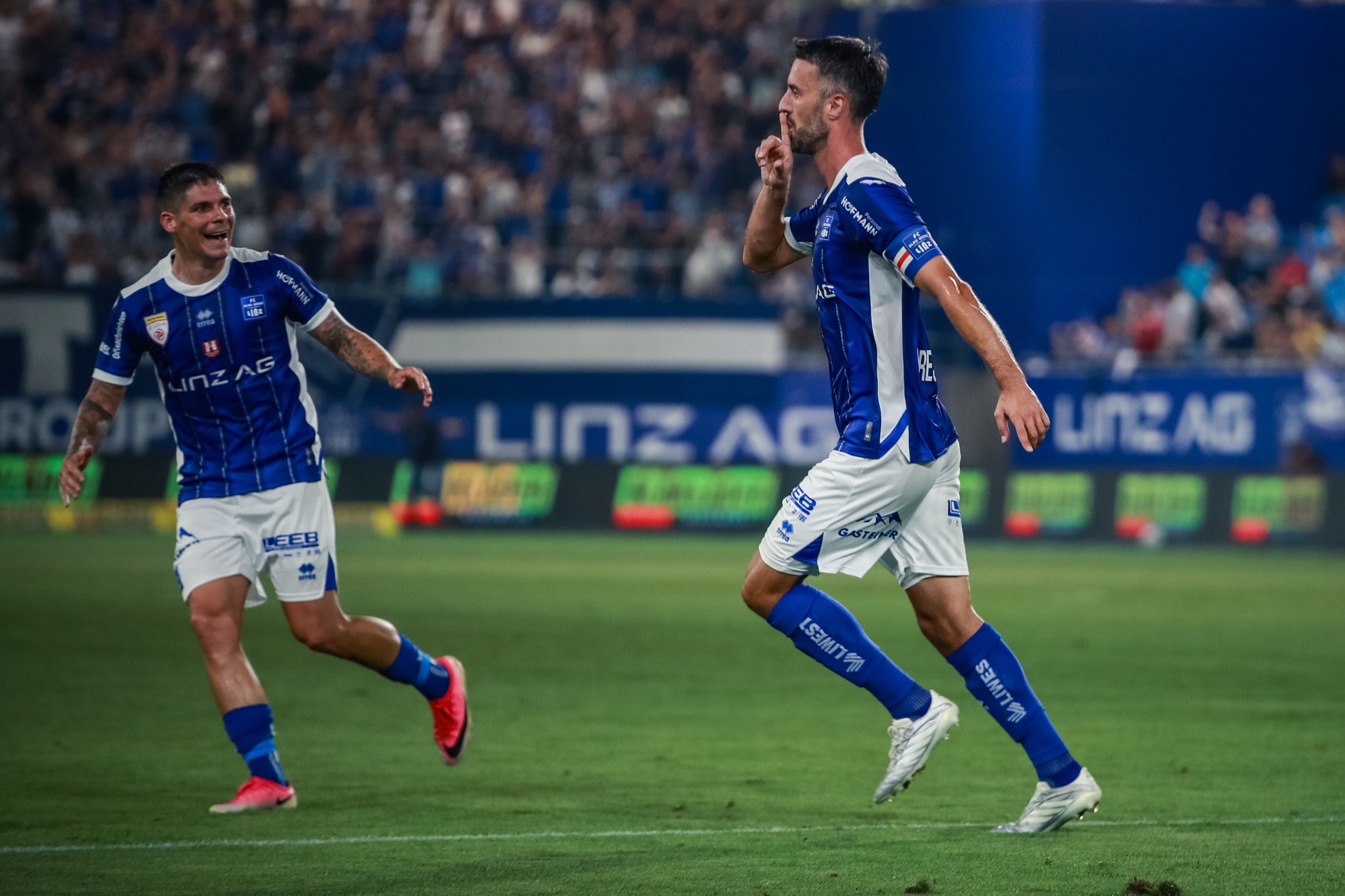 Zwei Fußballspieler von Blau Weiss Linz jubeln auf dem Spielfeld nach einem Tor.