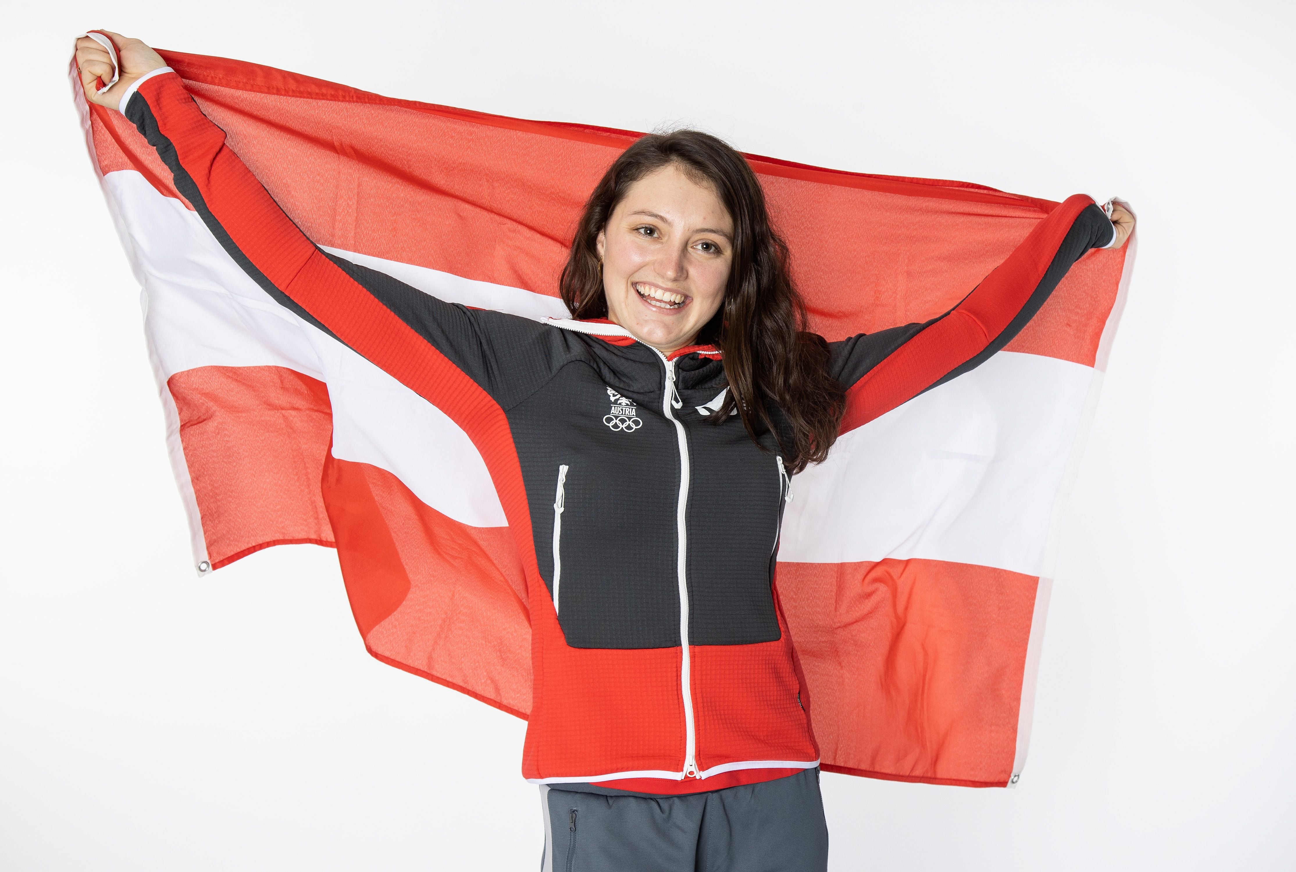 Frau mit österreichischer Flagge und olympischer Kleidung lächelt in die Kamera.