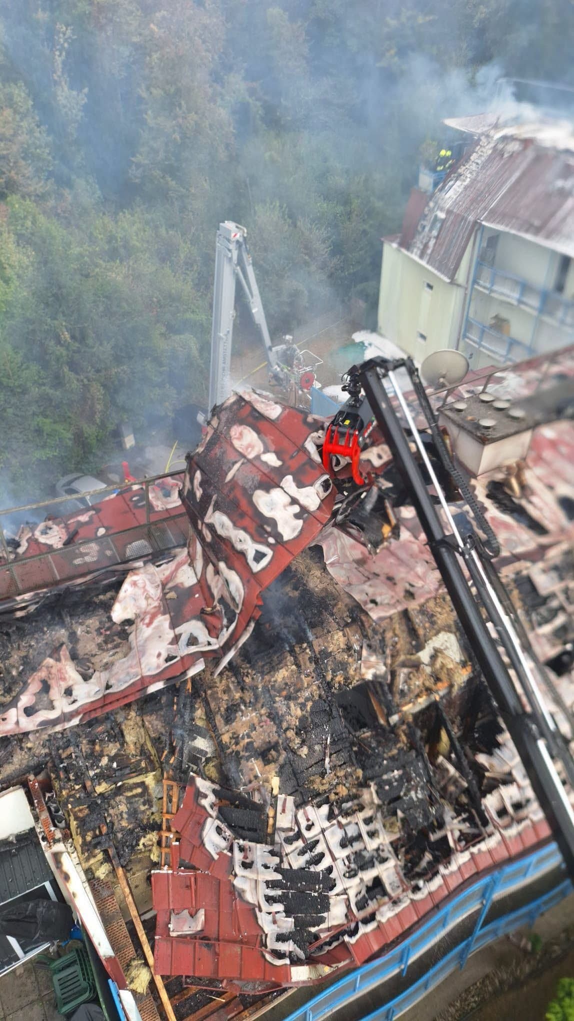 Ausgebranntes Hausdach mit Einsatz von Feuerwehrkränen nach einem Brand in Kematen.