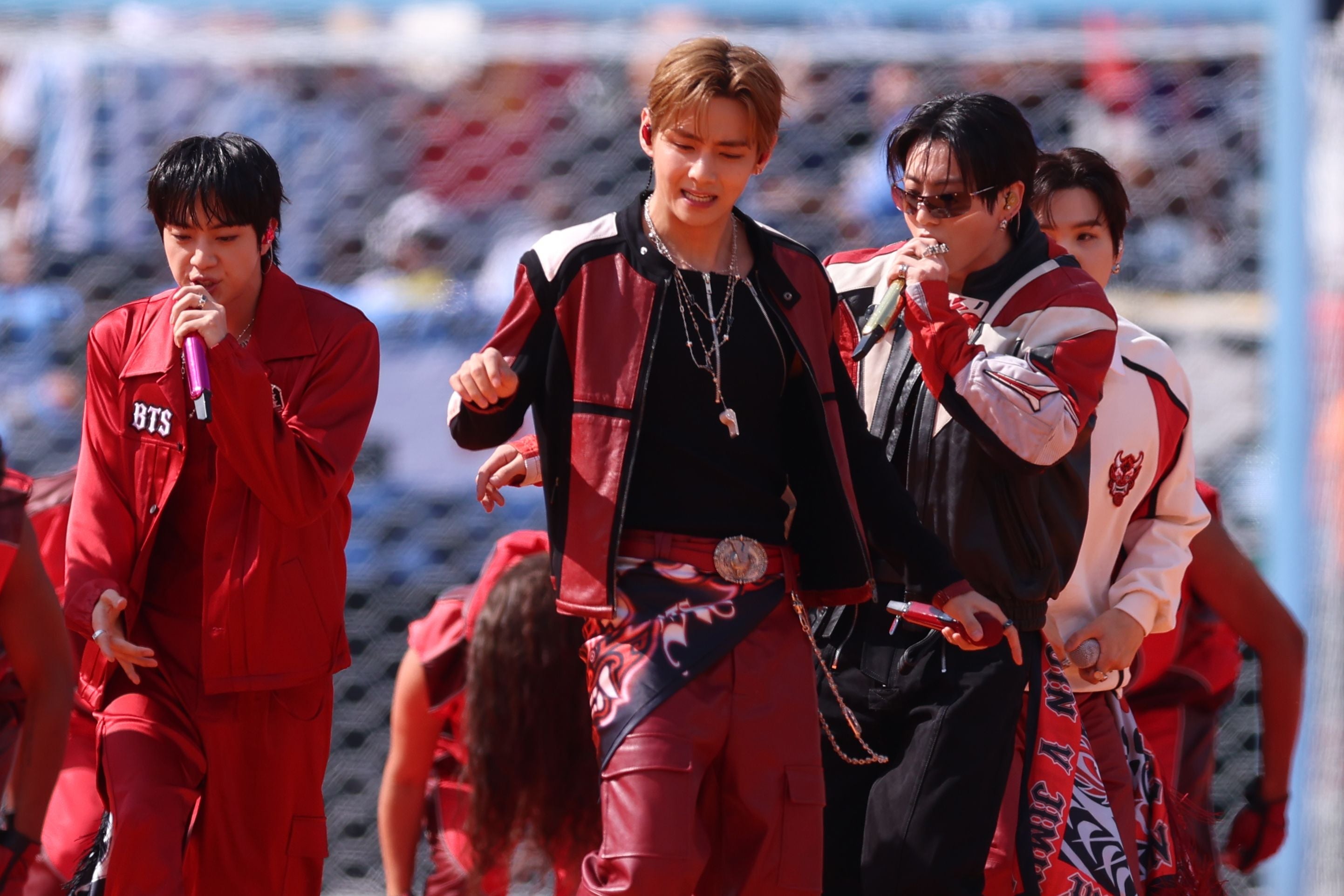 Mehrere Mitglieder von BTS treten in roten Outfits bei einer Halbzeitshow im Stadion auf.