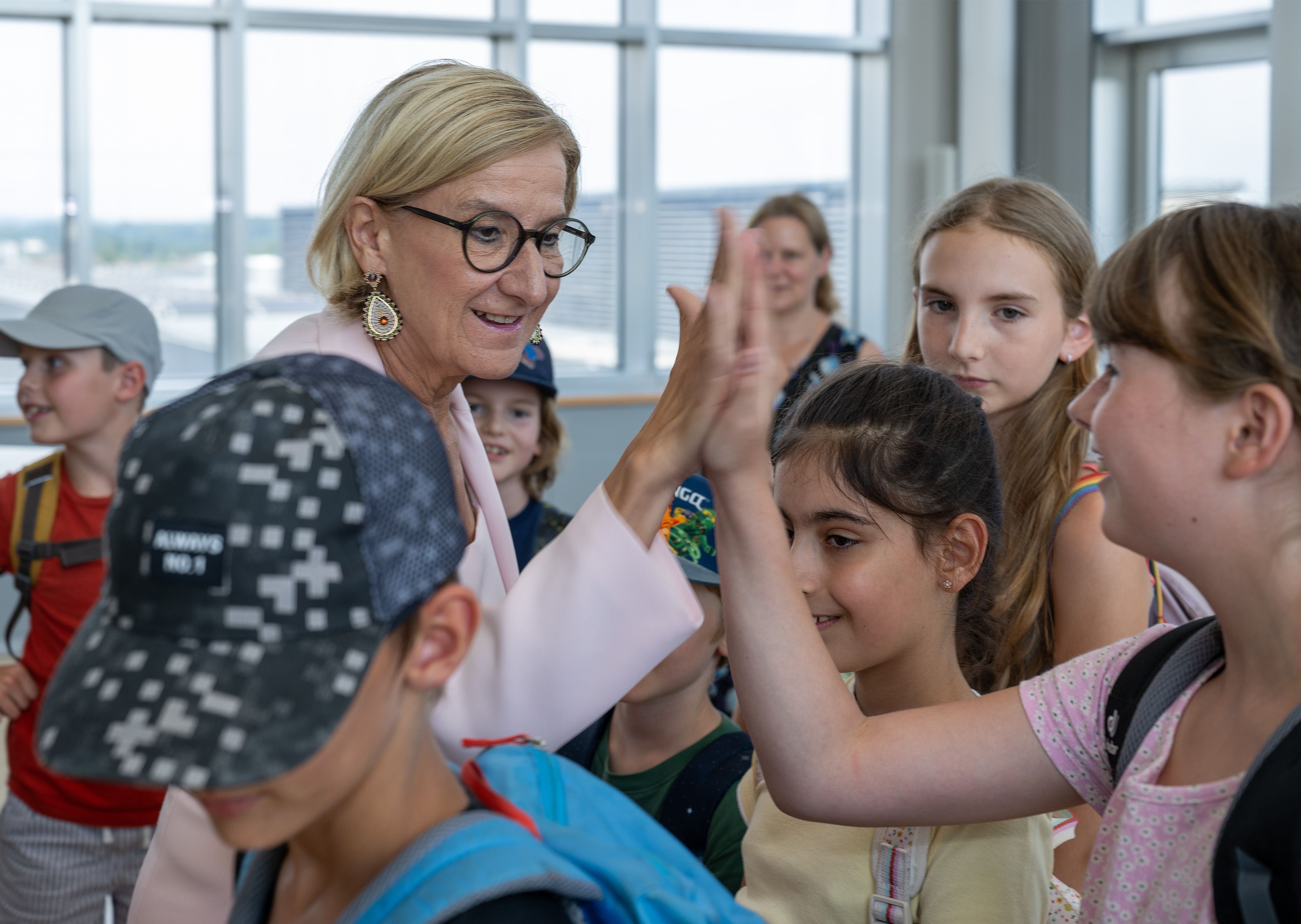 Eine Frau gibt mehreren Kindern bei einem Besuch in einem hellen Raum ein High-Five.